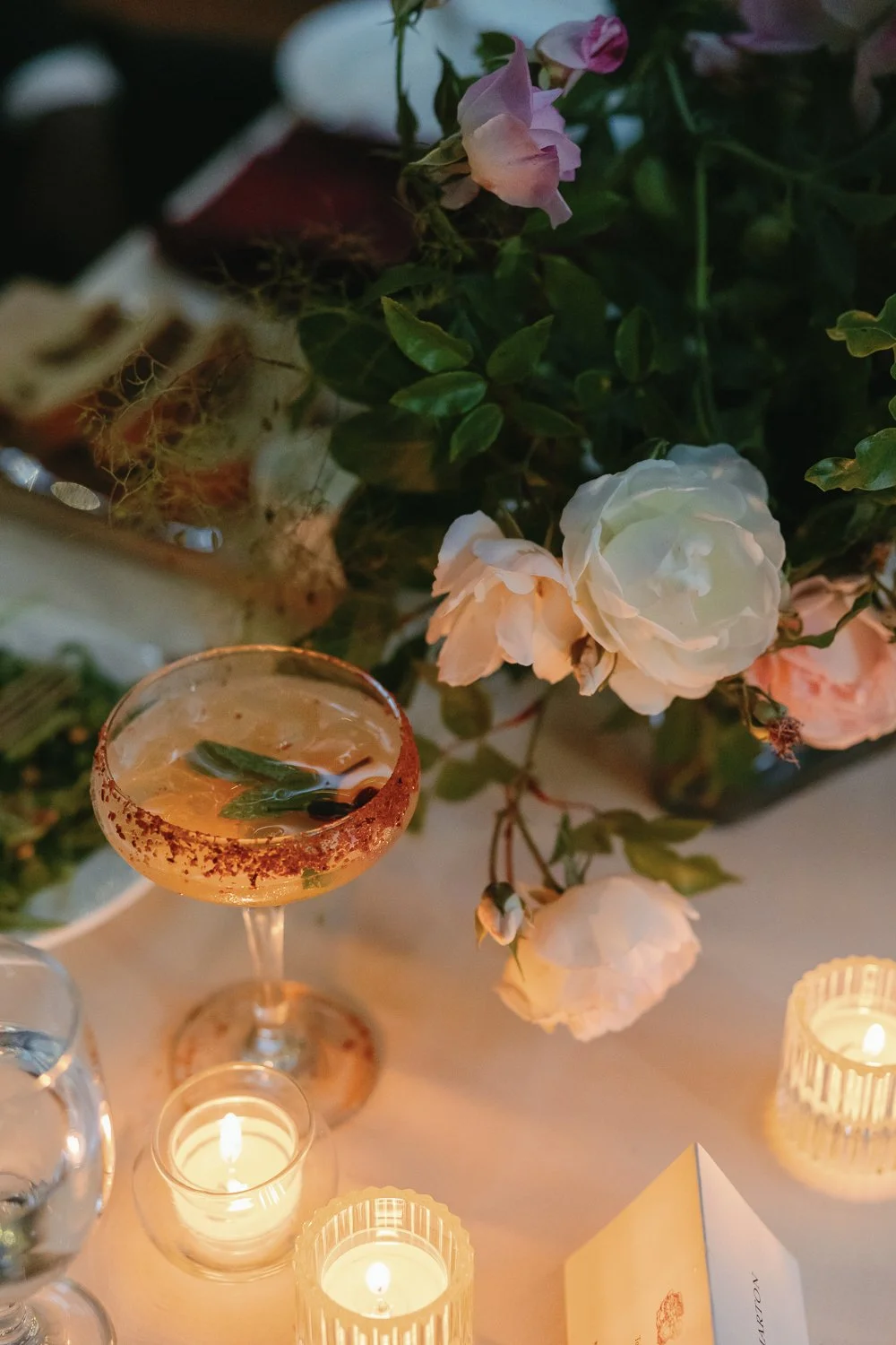 A table decorated with candles, roses, and a cocktail with mint leaves.