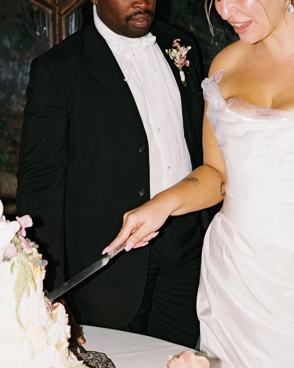 A couple, dressed in wedding attire, cutting a wedding cake together.