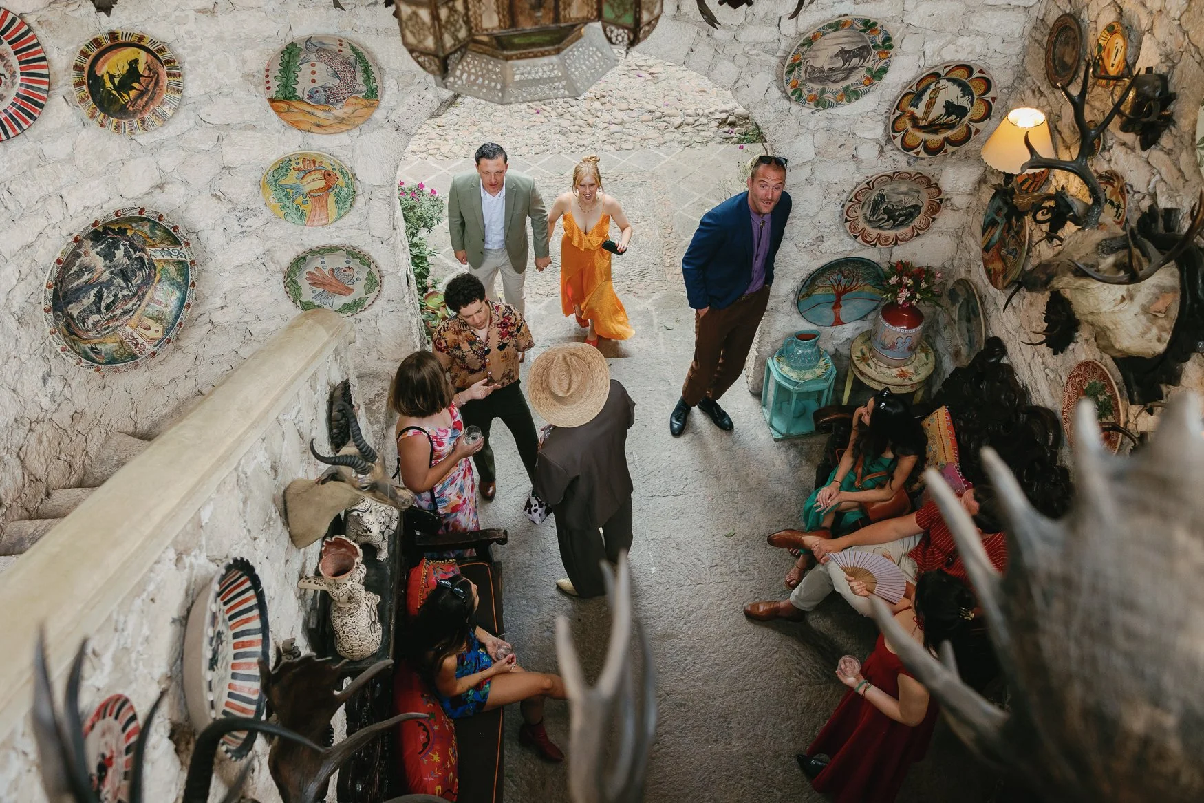 Group of guests gathered in a rustic stone welcome room decorated with colorful ceramic plates, pottery, antlers, and taxidermy.