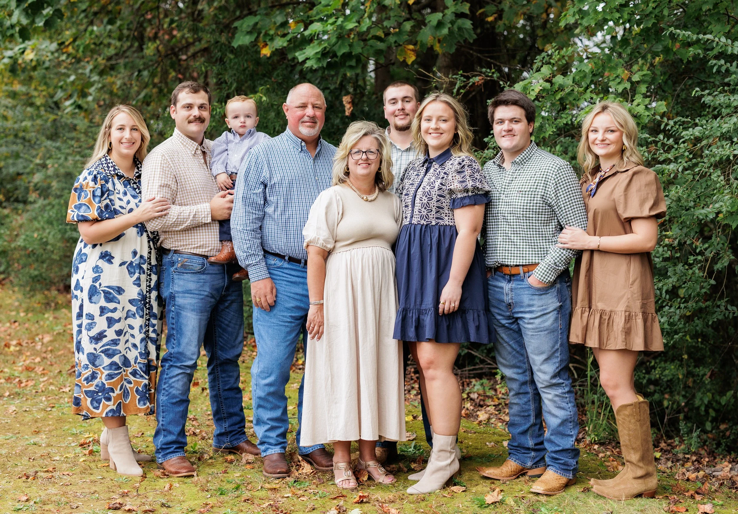 A large multi-generational family standing outdoors in front of green trees, smiling for a group photo.
