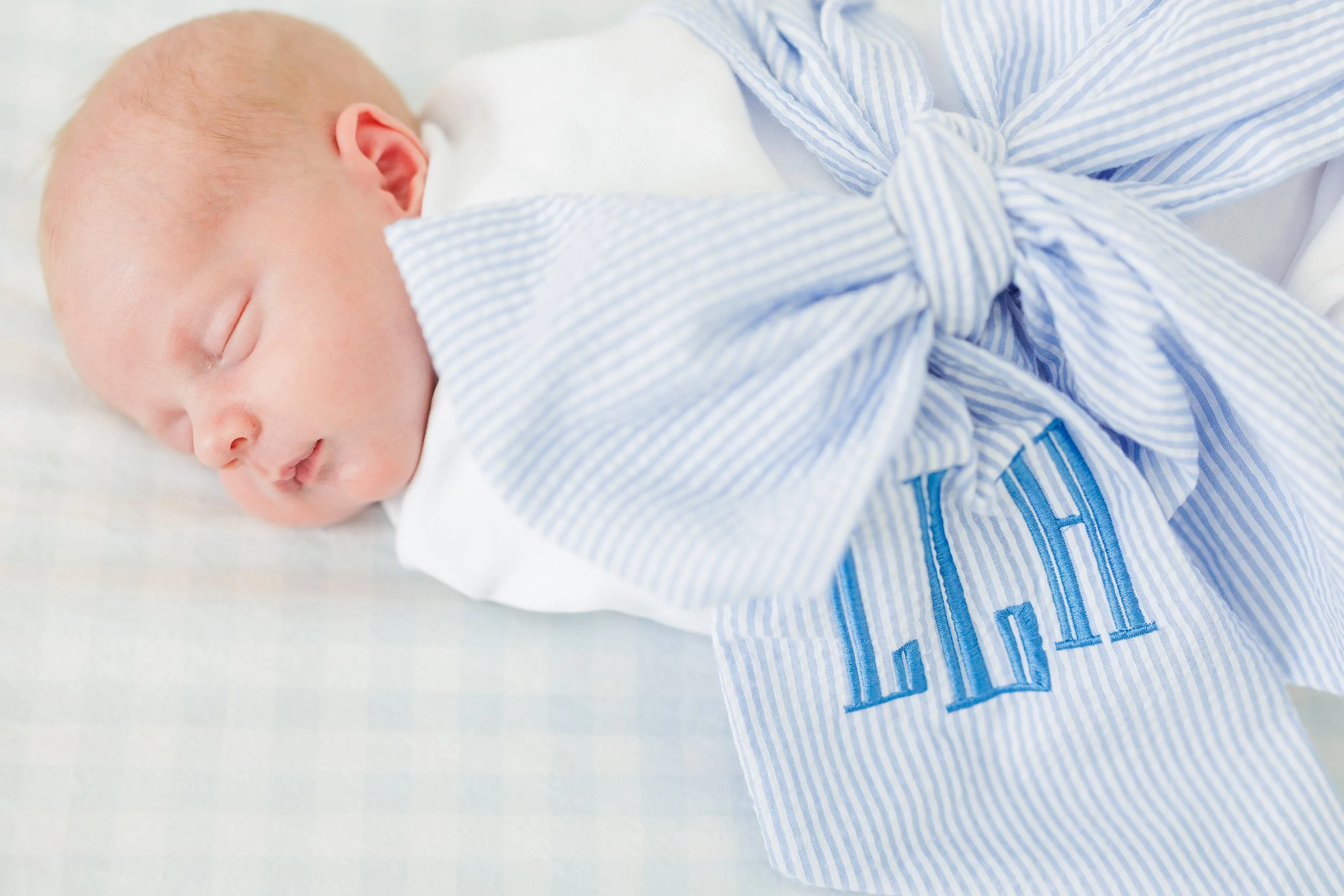Close-up of a sleeping newborn baby with a bald head, lying on a white surface, wearing a blue and white striped outfit.