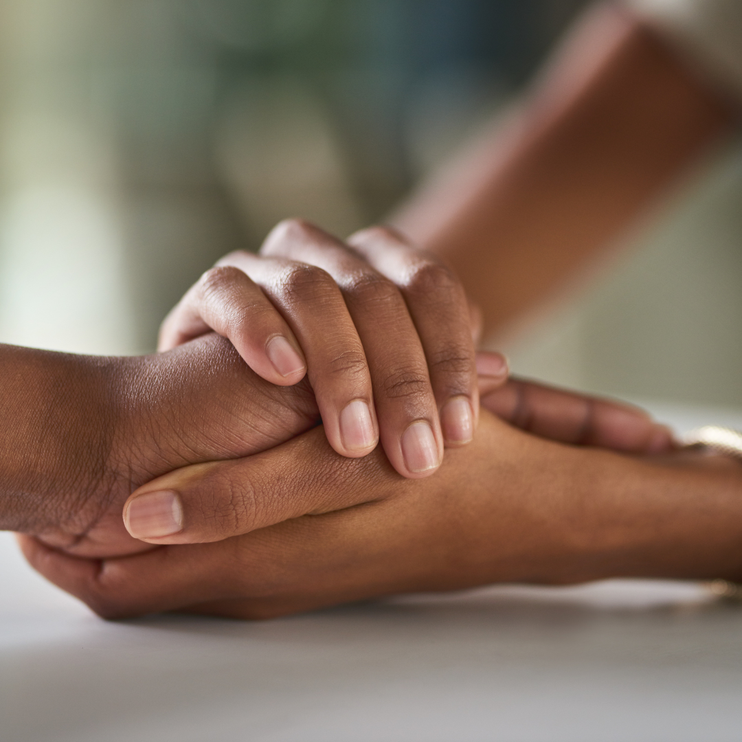 Two hands, one darker-skinned and one lighter-skinned, clasped together in a supportive gesture.
