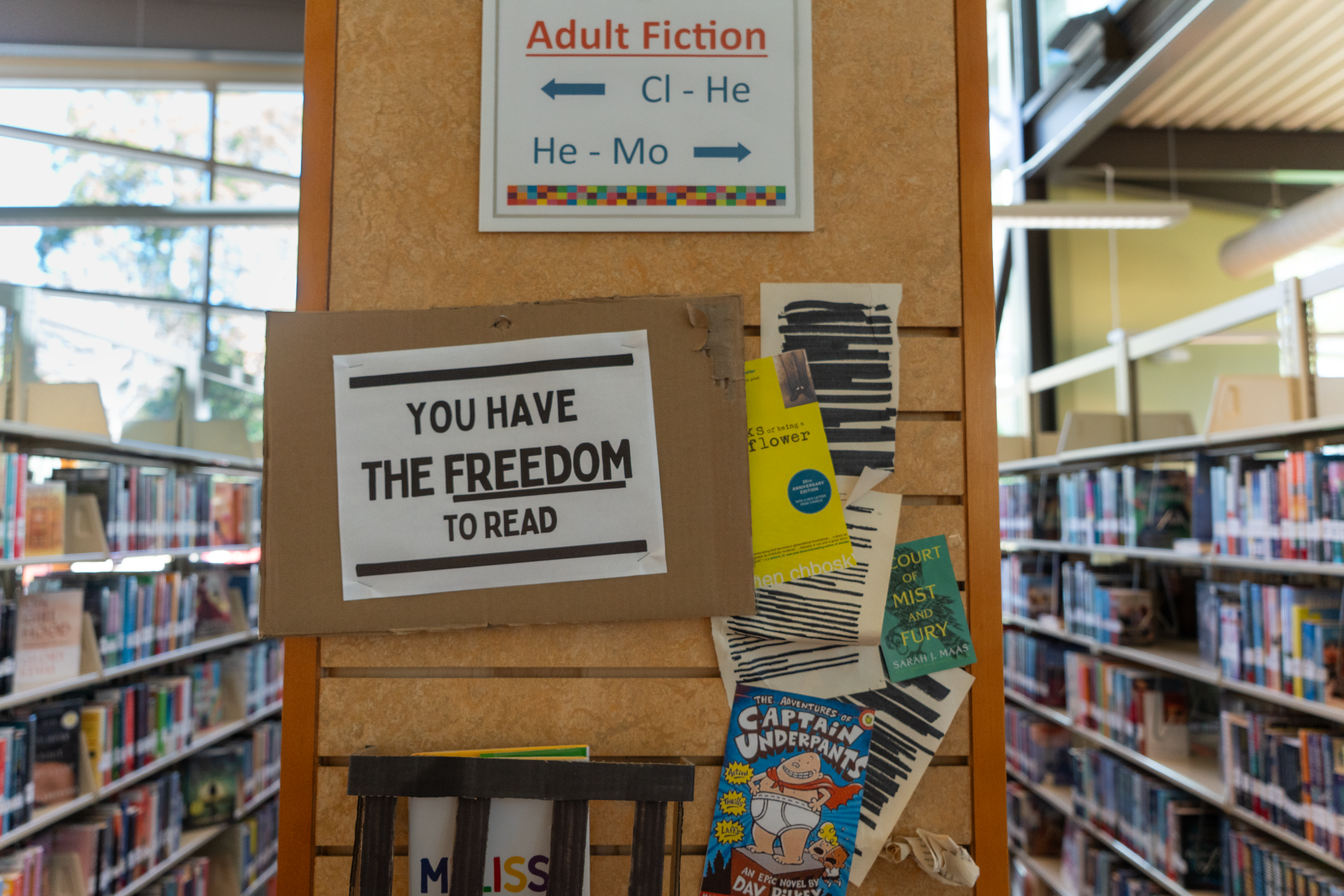 A sign on the end of a bookshelf that reads, "you have the freedom to read," accompanied by single pages with the text redacted by black marker, a copy of "Captain Underpants," and a copy of "The Perks of Being a Wallflower."