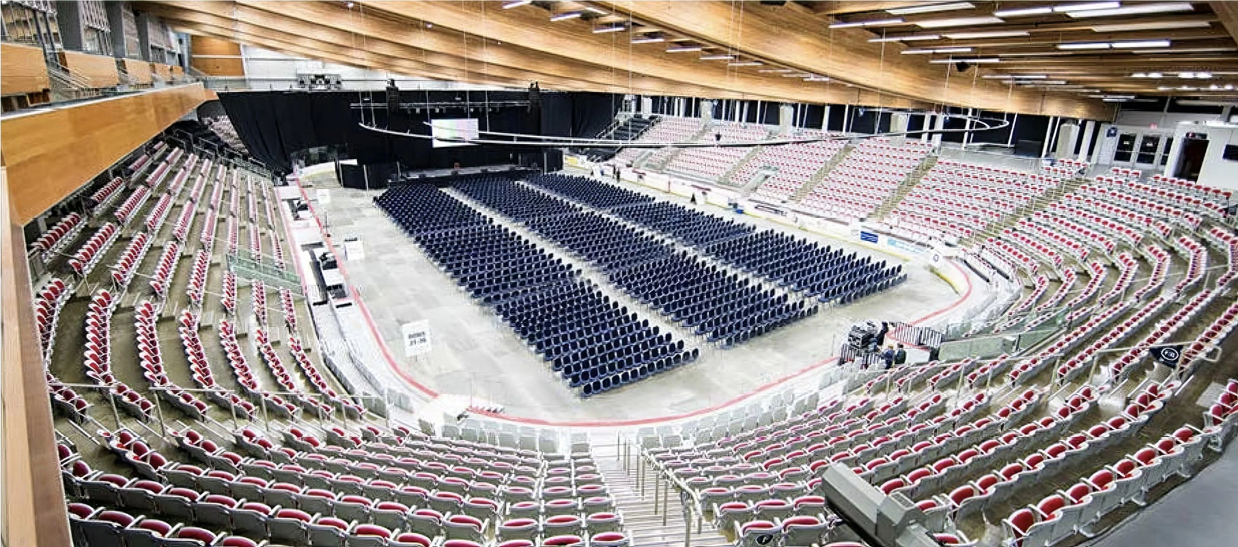Empty indoor arena with rows of red and white seats surrounding a large ice rink, set up for a hockey event.