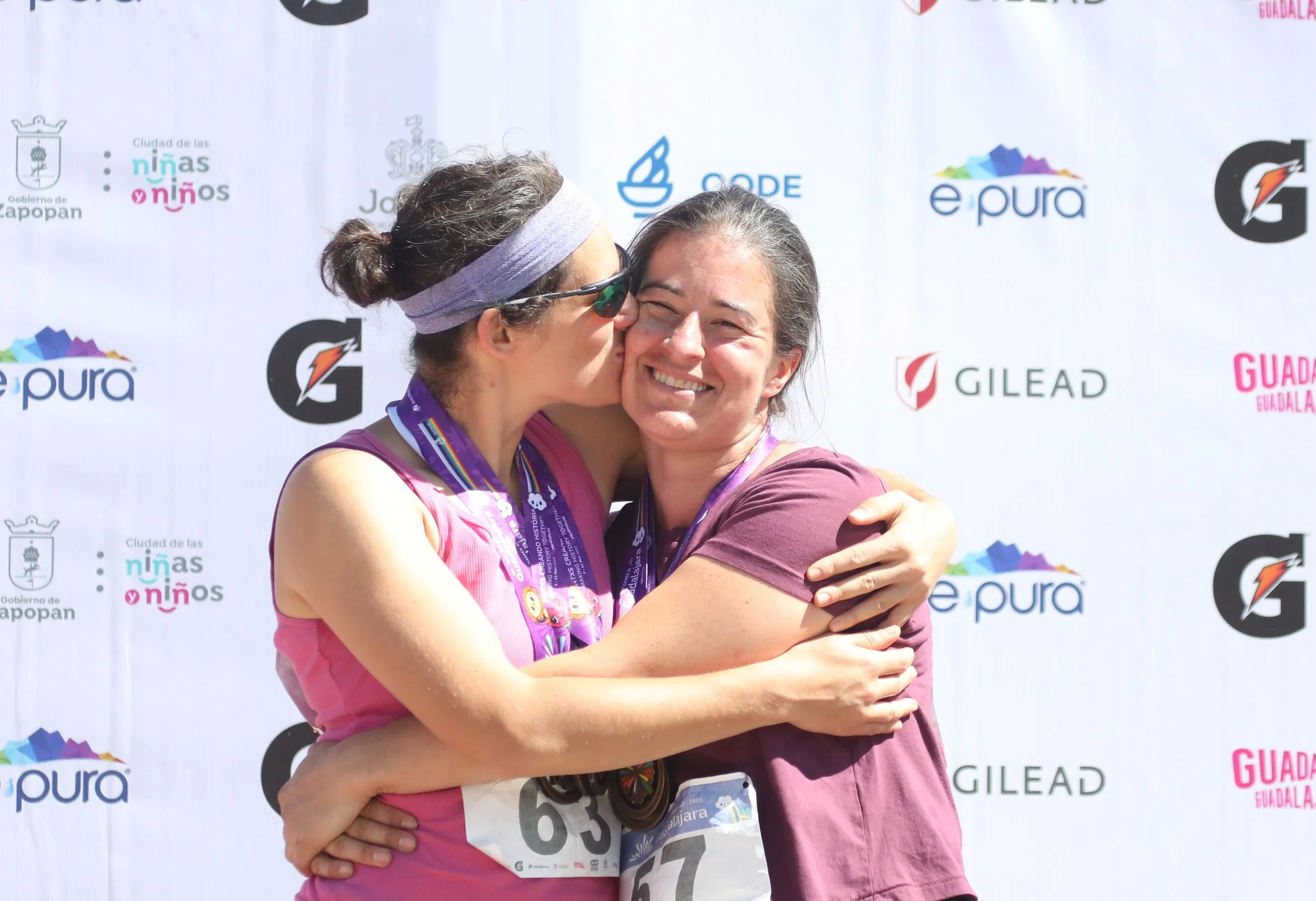 Anna Jaffe (Anna Sylvan-Jaffe Waldman-Brown) standing in front of a gay games banner with their partner at the track and field events.