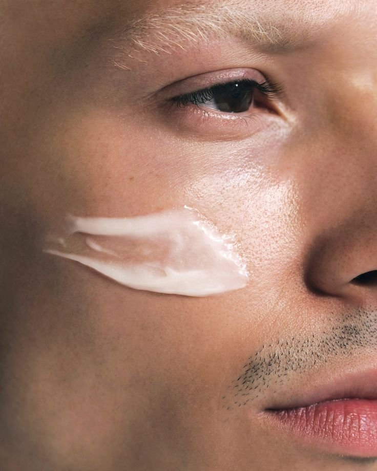 Close-up of a man's face with skincare cream applied to the cheek, focusing on the eye and facial hair.