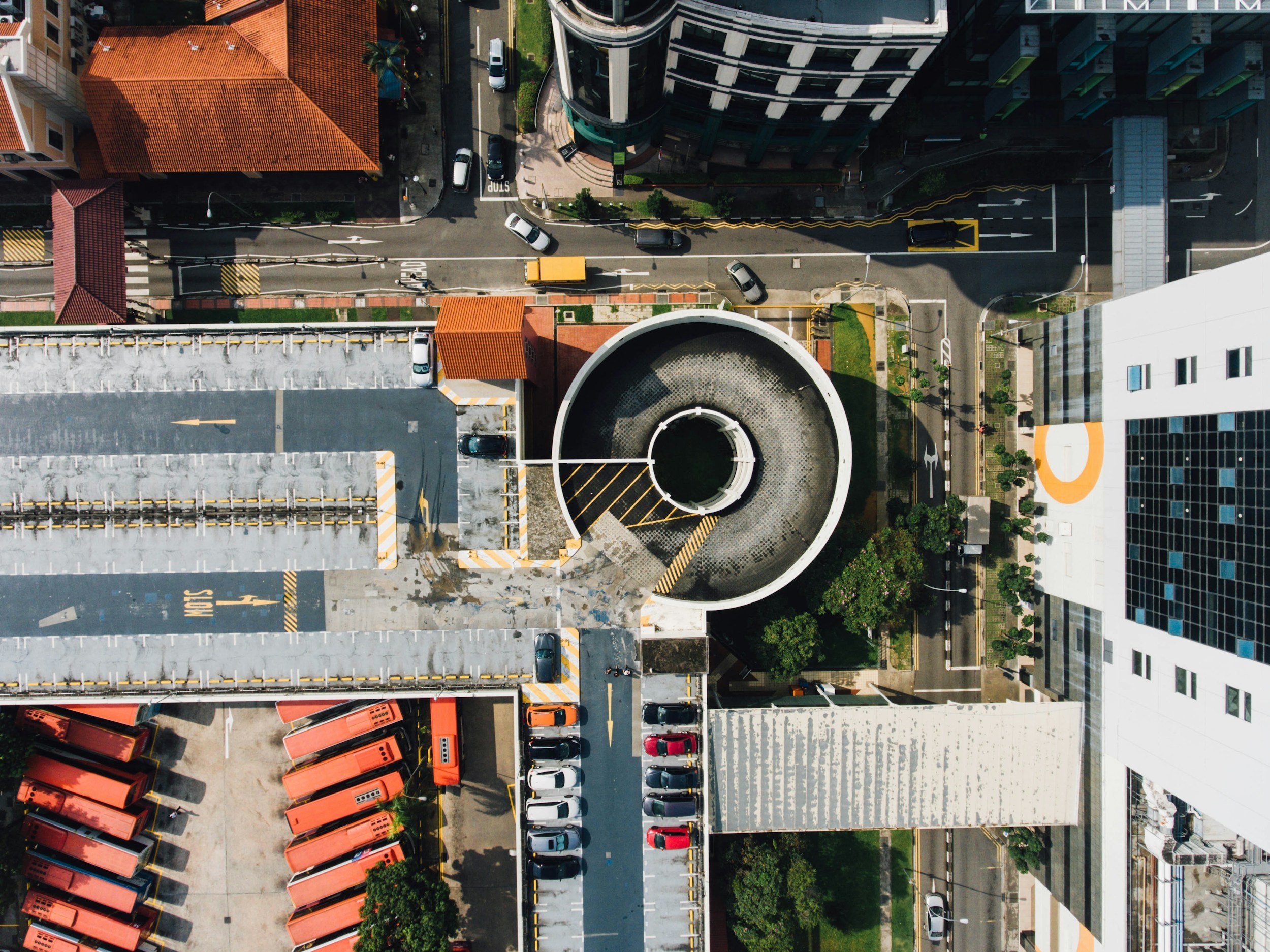 An aerial view of a city block showing parking lots, streets, and buildings, including a circular rooftop structure and surrounding urban infrastructure.