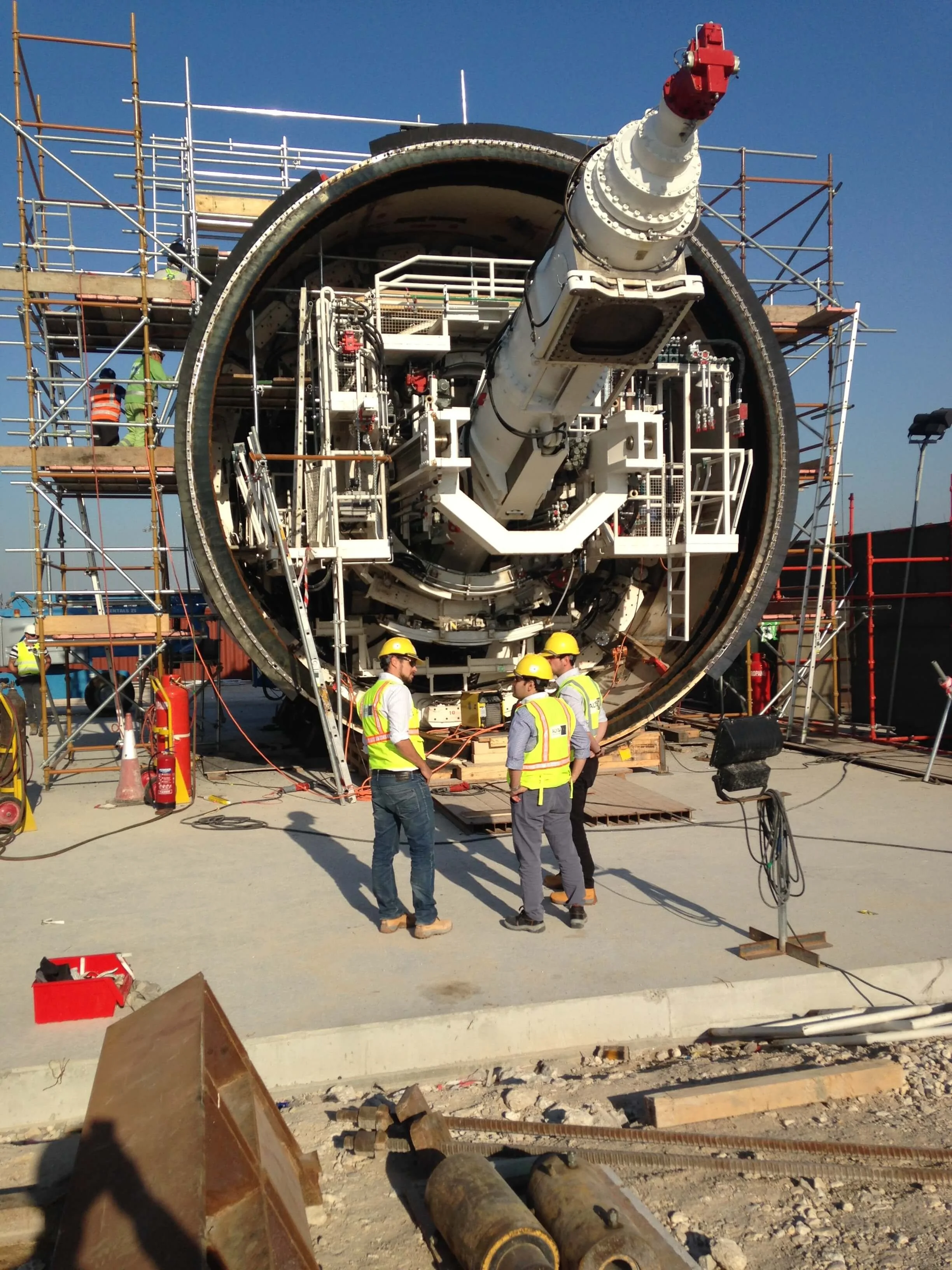 Engineers in safety gear inspecting the large underground tunnel boring machine (tbm) at the Doha Metro Goldline construction site.