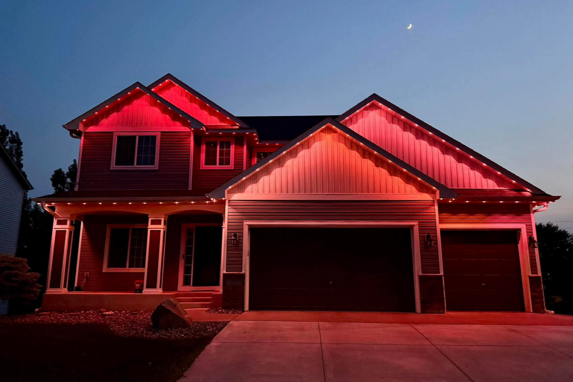 Permanent LED roofline lighting on a two-story home glowing brilliantly against the night sky