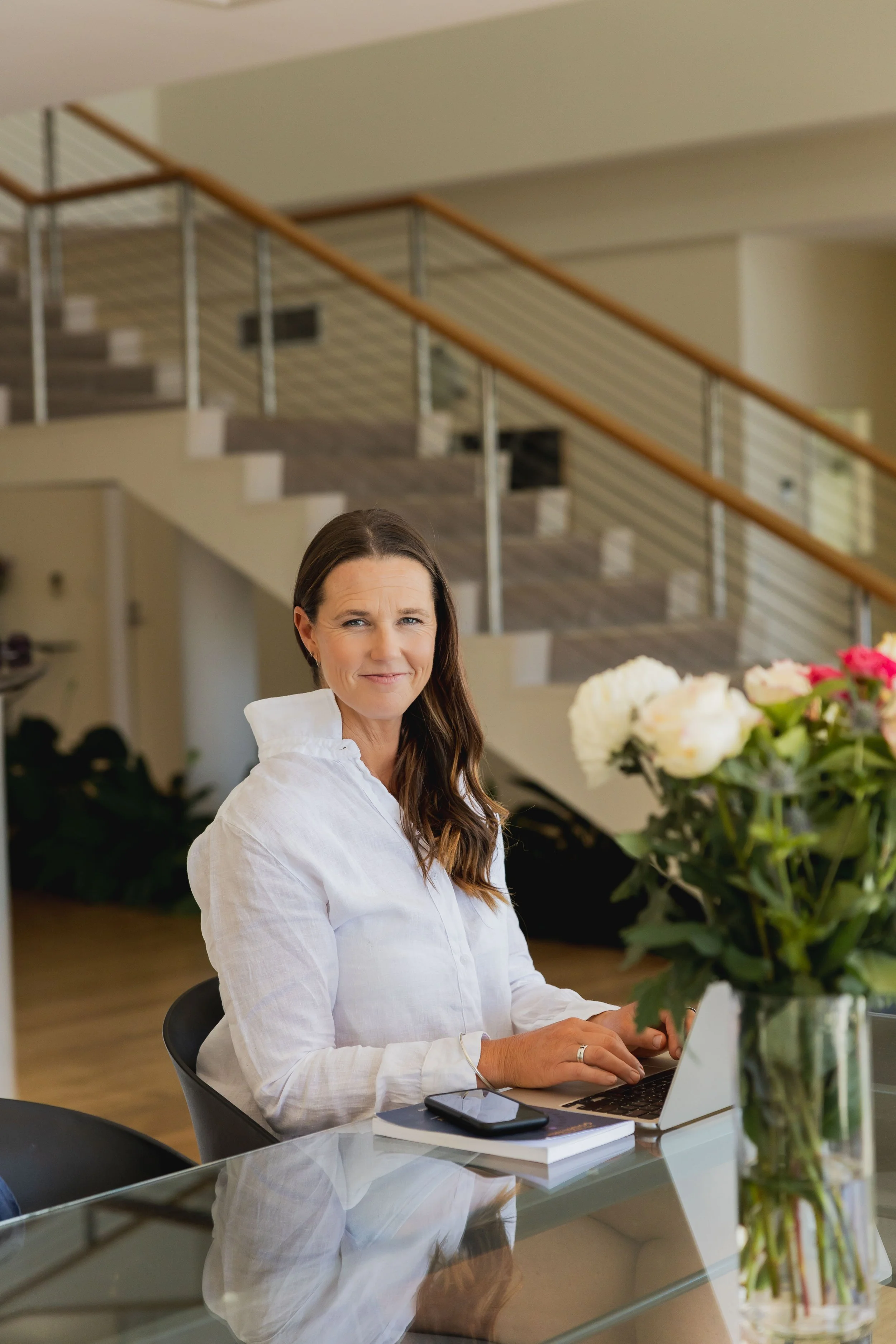 Founder Lucy Peel, Human Design specialist, working on a laptop at a glass desk with white and pink roses.