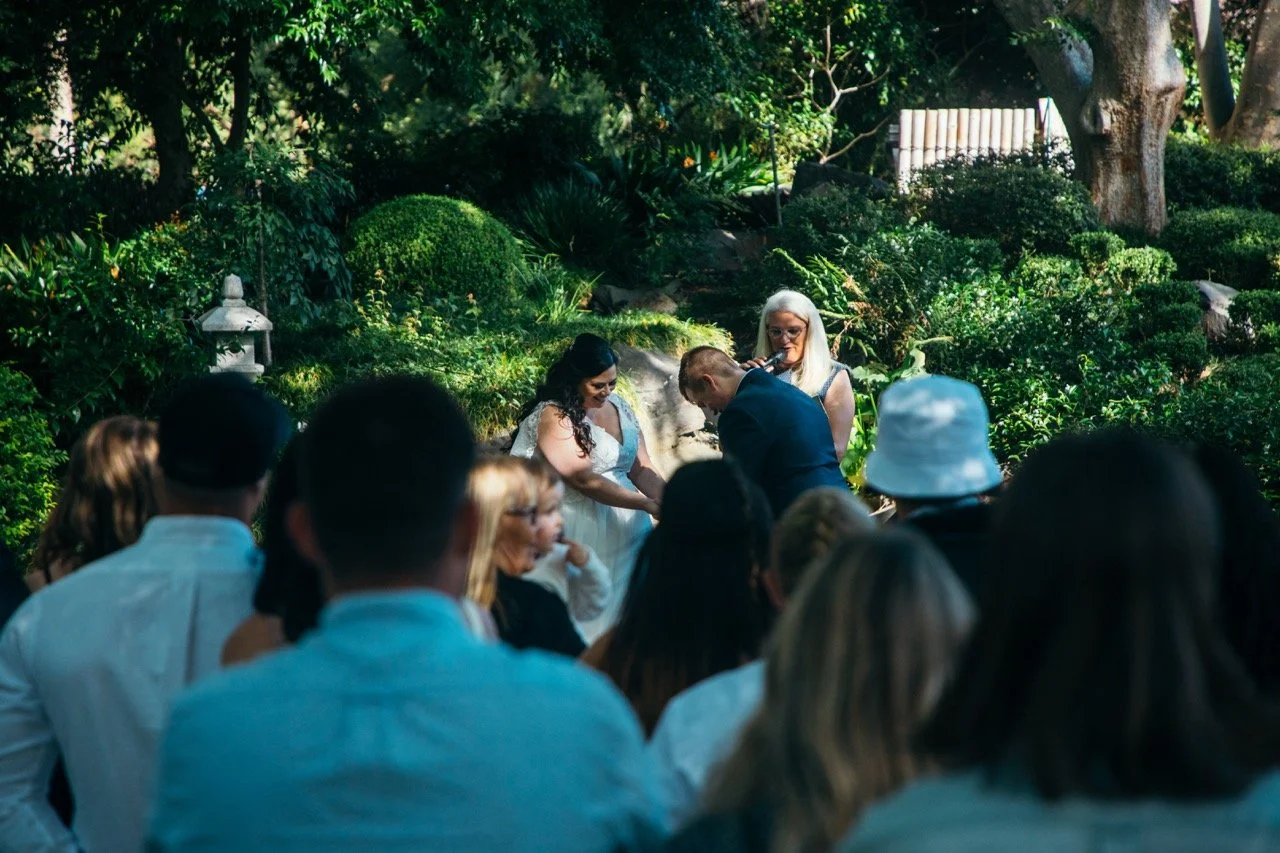 A wedding ceremony outdoors in a lush garden with the couple exchanging vows, surrounded by guests.