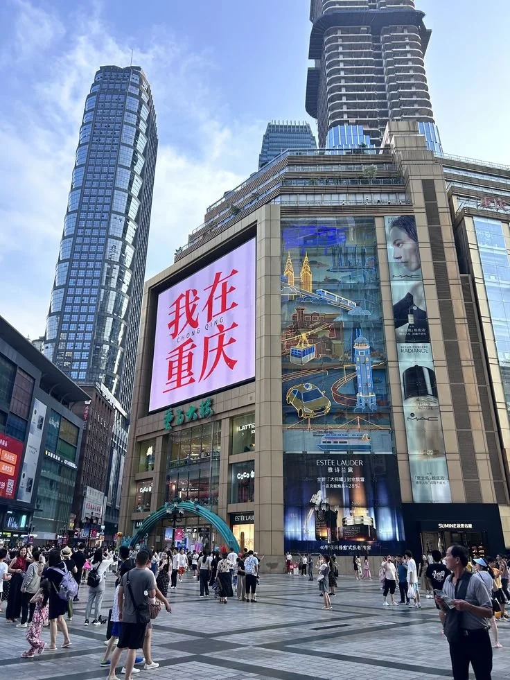 Crowd of people gathered in a busy urban shopping district with tall skyscrapers, large electronic billboards, and retail stores.