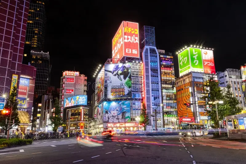 A vibrant cityscape at night with illuminated billboards and neon signs on tall buildings, busy streets with moving vehicles, and a few trees lining the sidewalks. Learning Expedition