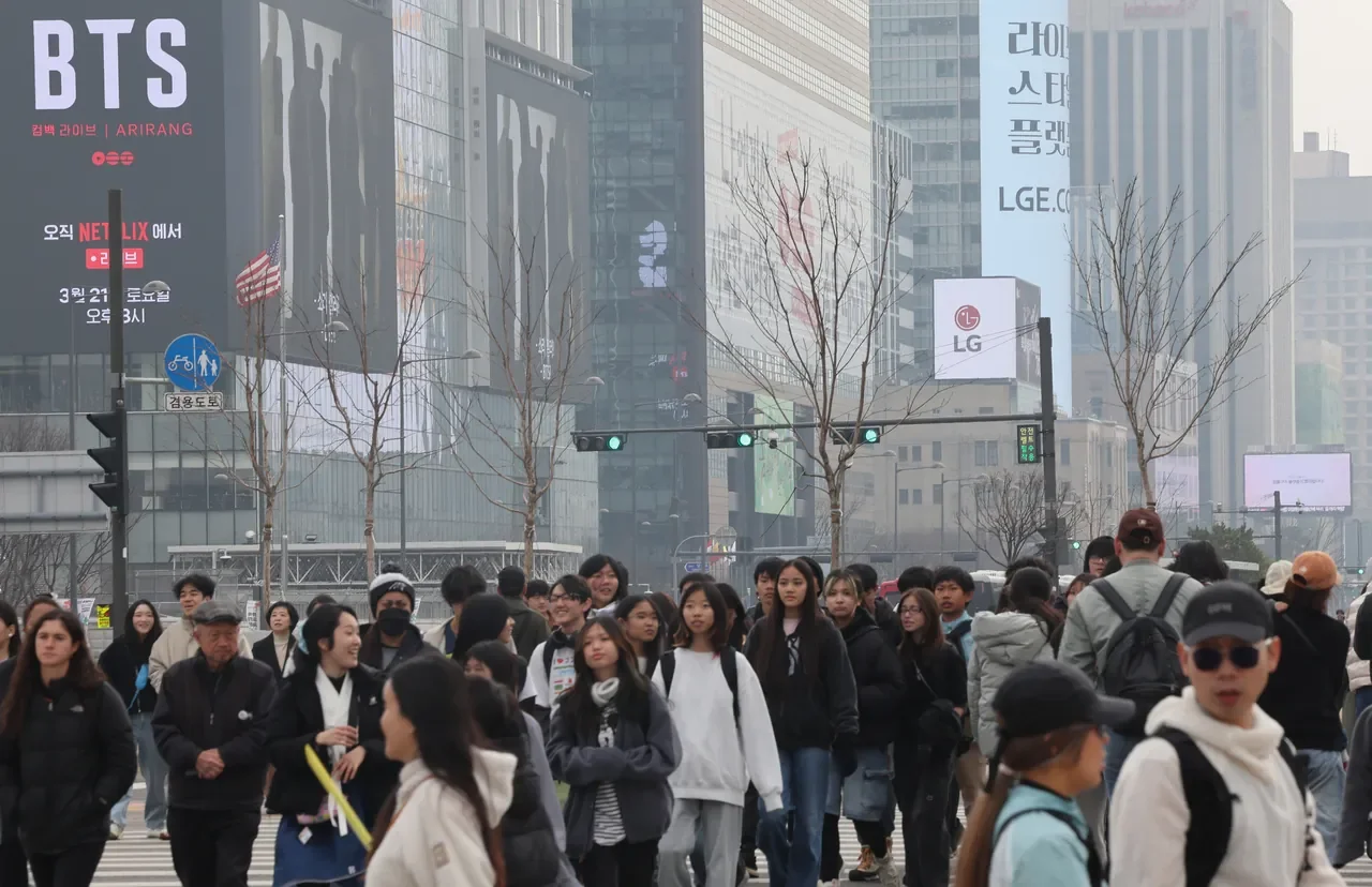 Pedestrians near Gwanghwamun Square in Seoul with a BTS comeback concert billboard behind them, showing culture-led demand