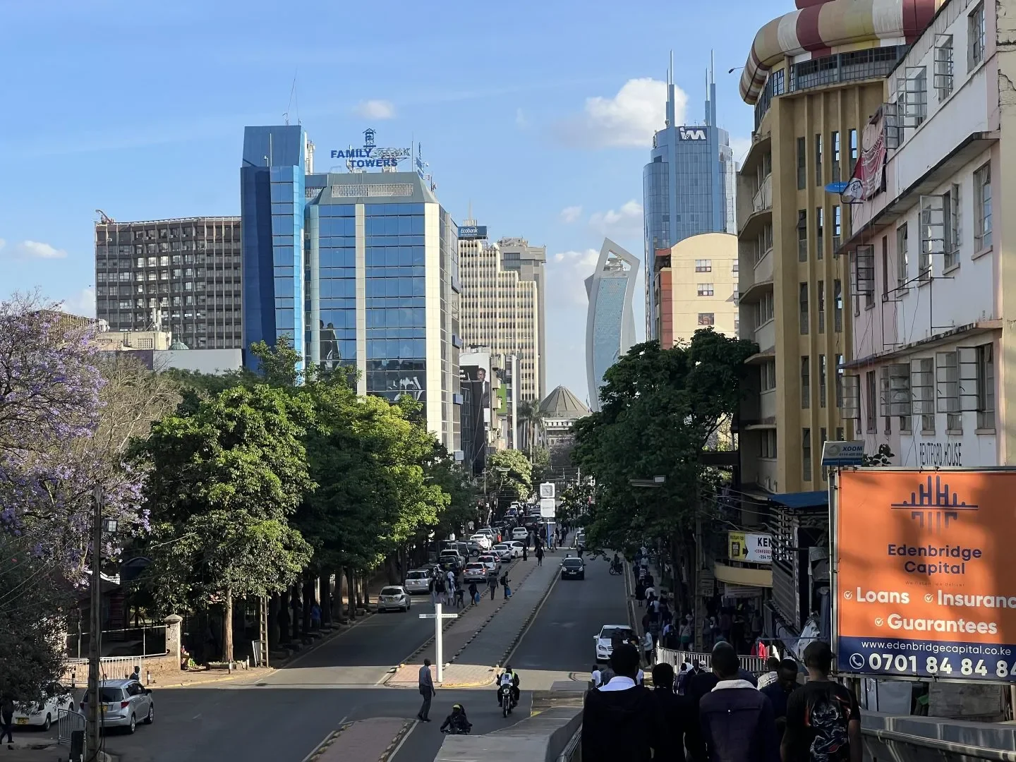 City street scene with people walking, cars parked along the sides, and tall modern skyscrapers in the background." Learning Expedition