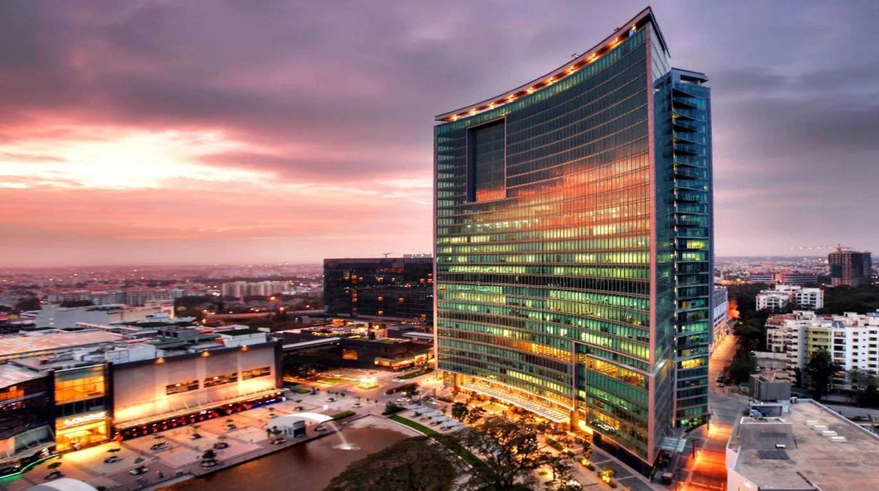 A tall, modern glass office building reflecting the colorful sunset sky stands in an urban area surrounded by other buildings and parking lots. Learning Expedition