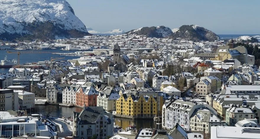 Snow-covered town with colorful buildings near water, surrounded by mountains in the background. Learning Expedition