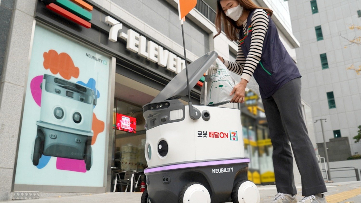 A Neubility autonomous delivery robot outside a 7-Eleven store in South Korea, with a store employee loading a delivery bag