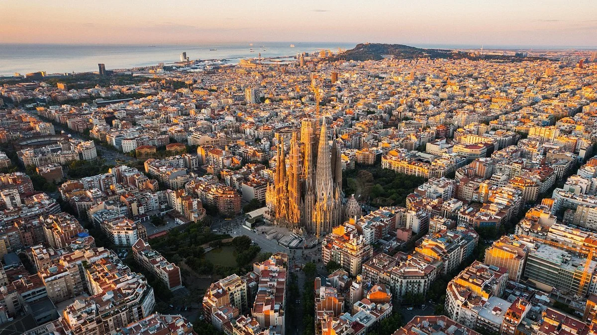 Aerial view of Barcelona city with Sagrada Familia basilica in the center and the coastline in the background, during sunset. Learning Expedition