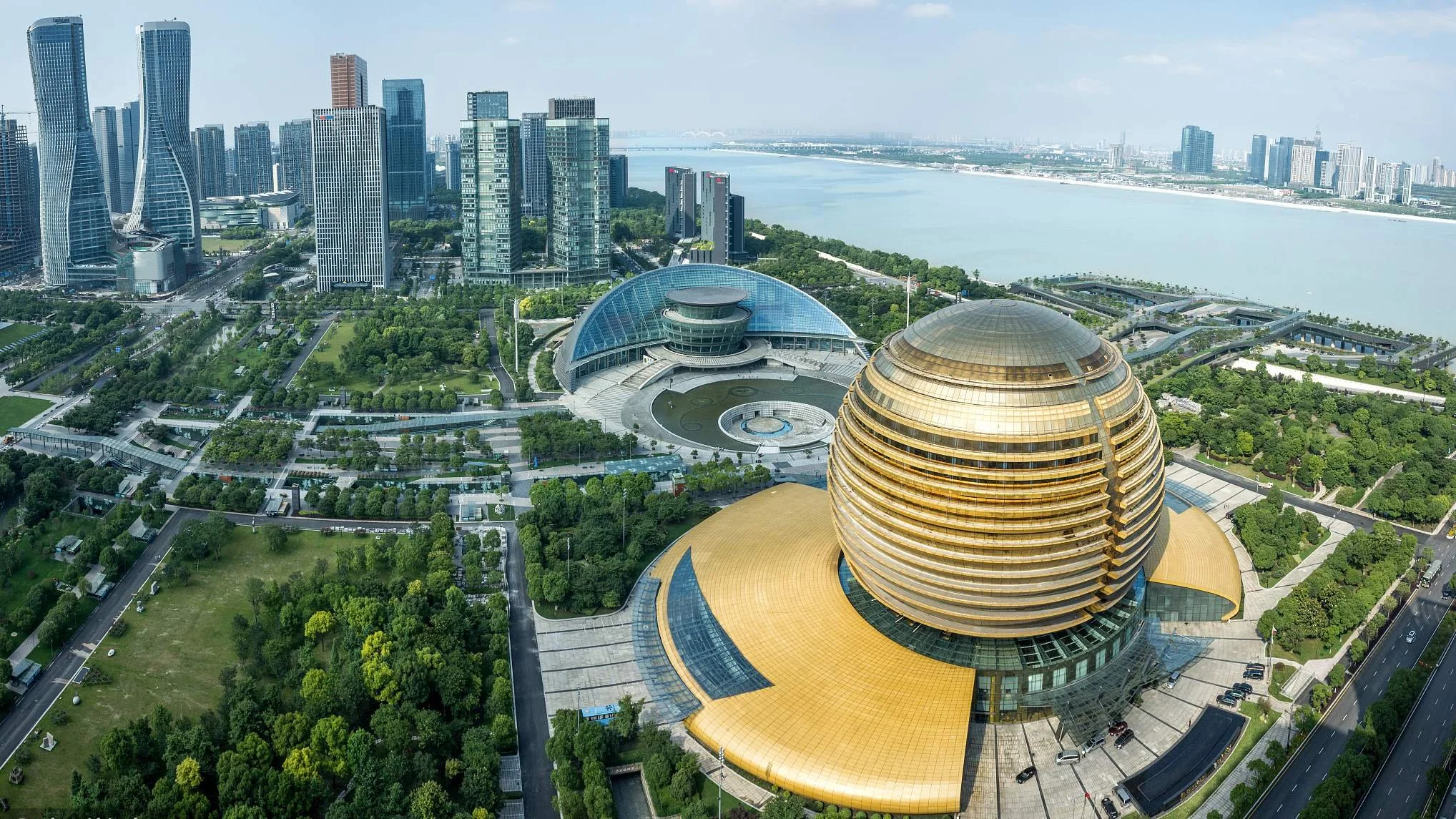 Aerial view of a modern cityscape with tall skyscrapers, green parks, and a large, golden, spherical building near a body of water. Learning Expedition