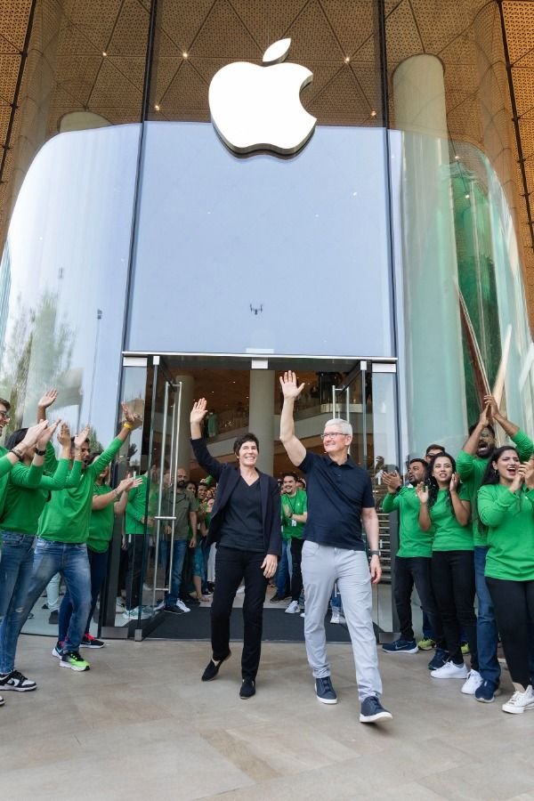 Celebration outside an Apple Store with employees in green shirts greeting a man and woman as they walk out, waving.