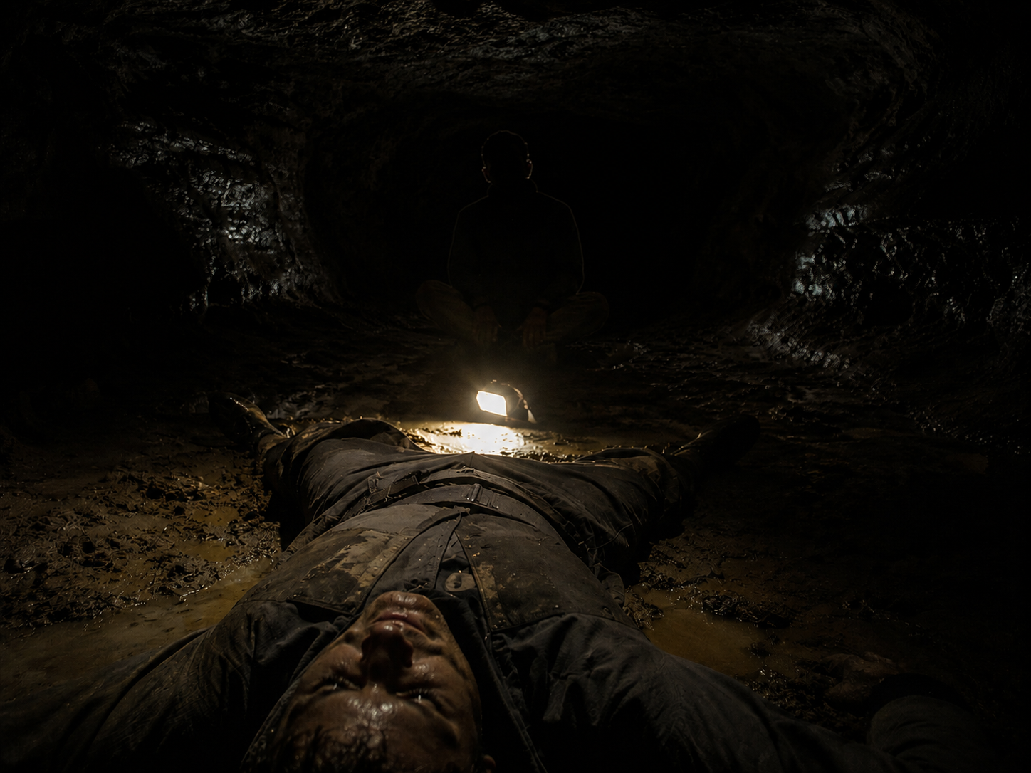 Ronan lying prone while Rusty sits waiting for Ronan to wake up in a dark cave