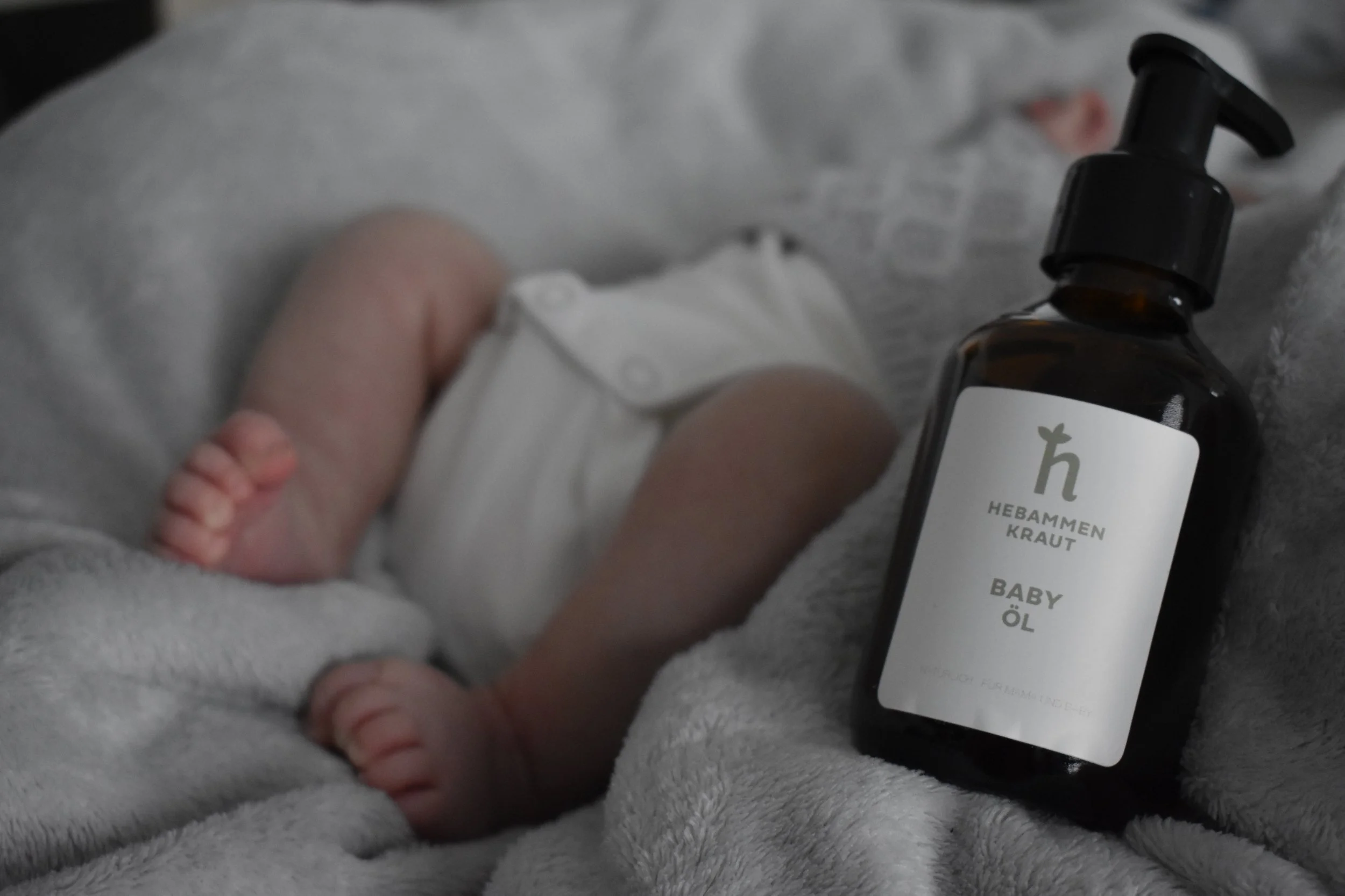 Eine Hand hält eine Flasche mit ätherischem Öl für Babys, auf einer weichen, hellgrauen Oberfläche.