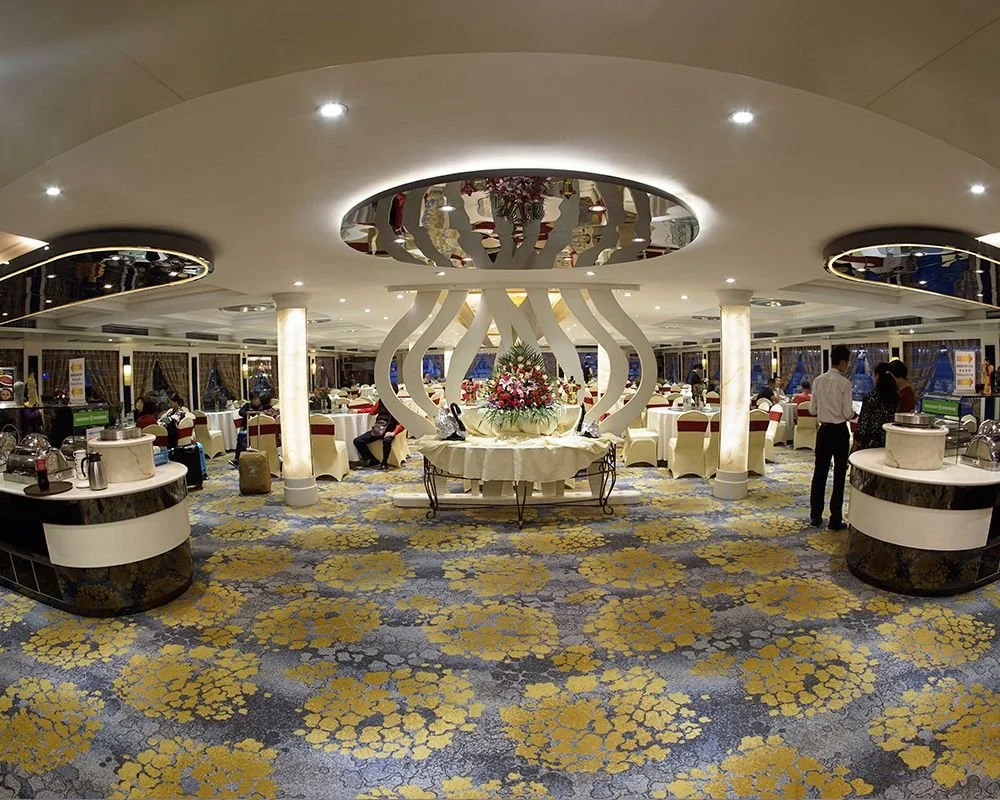 Interior of a restaurant or banquet hall with round tables, floral centerpiece, and people dining.