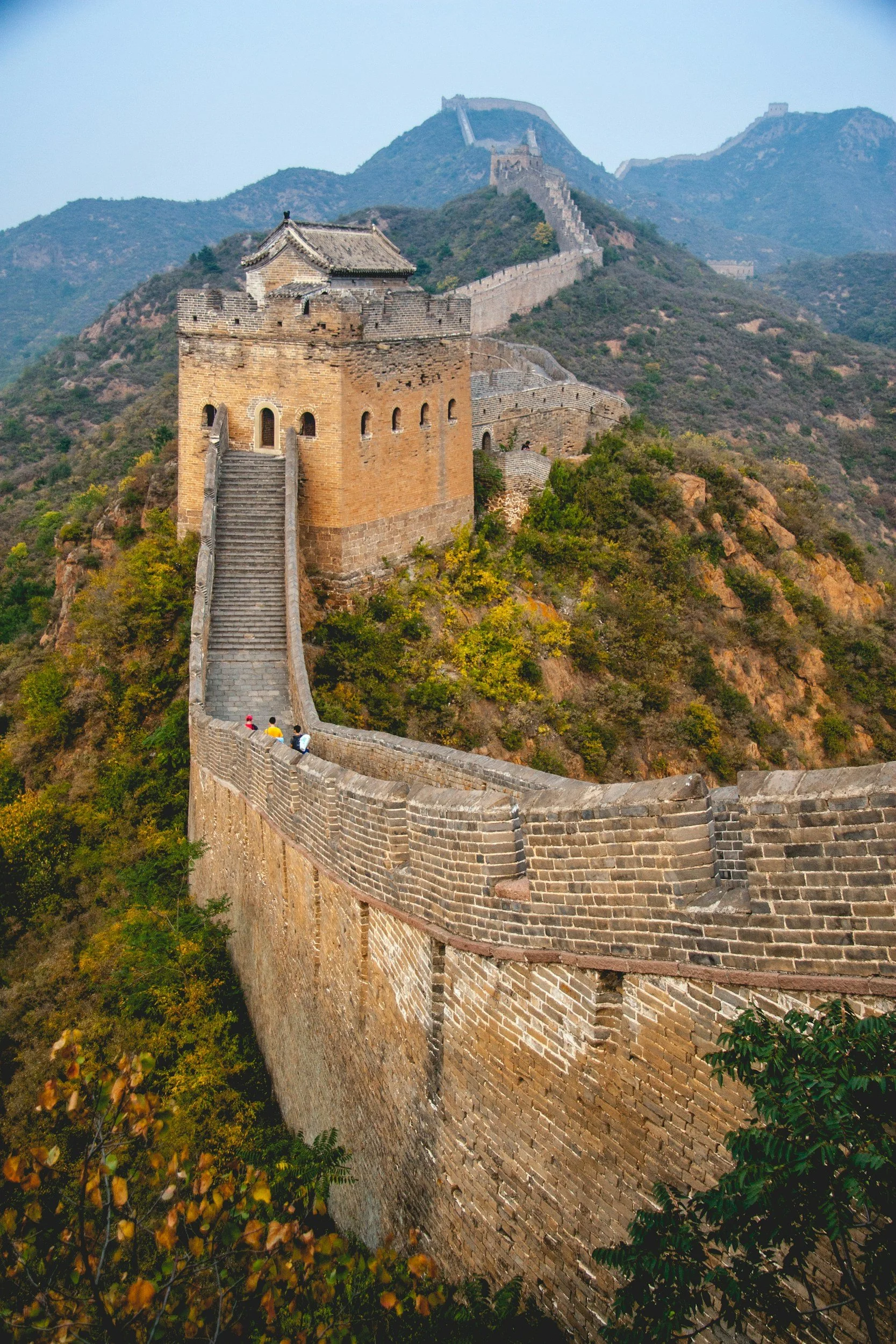 The Great Wall of China extending over mountains and hills with a few tourists walking along it.