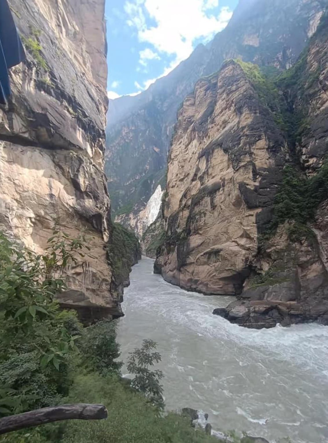 A river flowing through a deep canyon with steep, rocky cliffs on either side under a partly cloudy sky.
