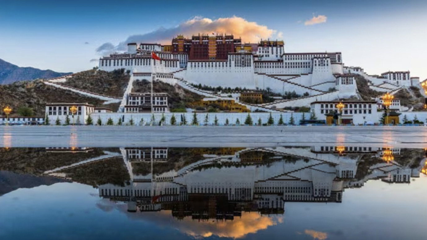 The Potala Palace in Lhasa, Tibet, reflected in a body of water with a clear sky and mountains in the background.