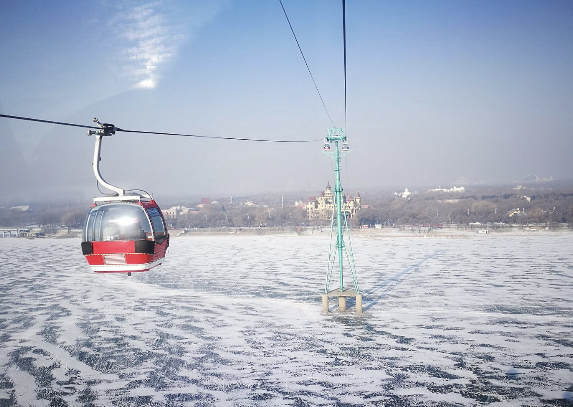A red and white gondola lift chair hanging from cable over a snow-covered landscape with a castle in the distance.