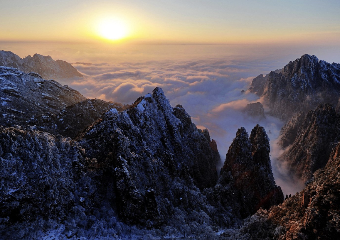 Snow-covered mountain peaks at sunrise with clouds in the valley below.