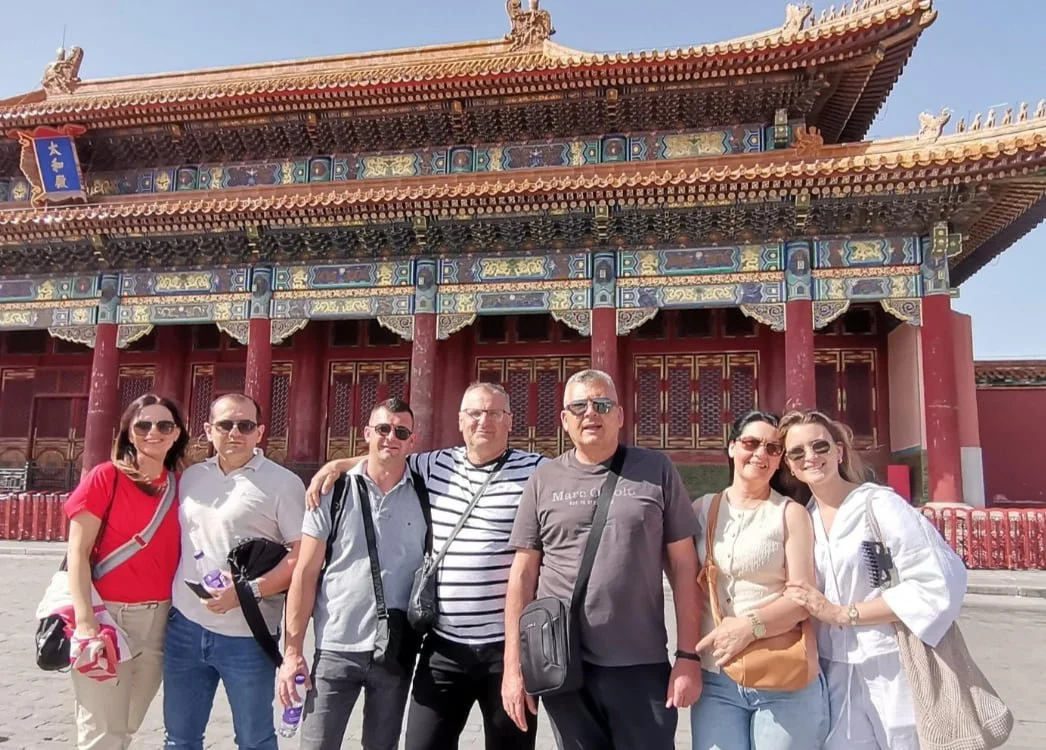 Group of seven tourists standing in front of a traditional Chinese building with ornate architectural details and a red exterior.