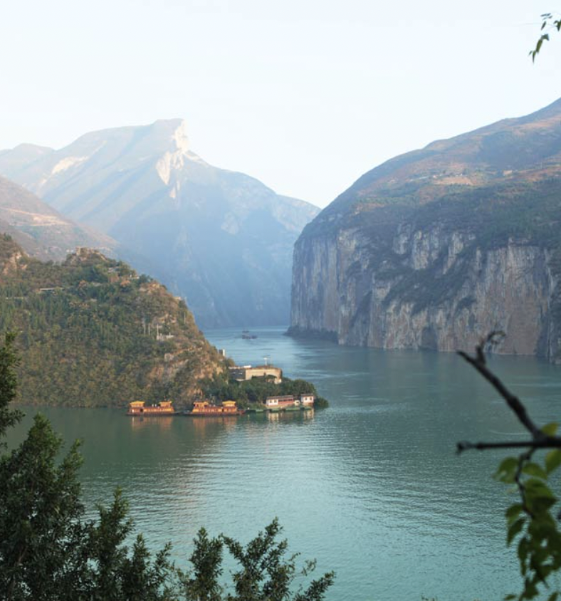 Sunset over a river with lush green trees on the left and tall, misty mountains in the background.