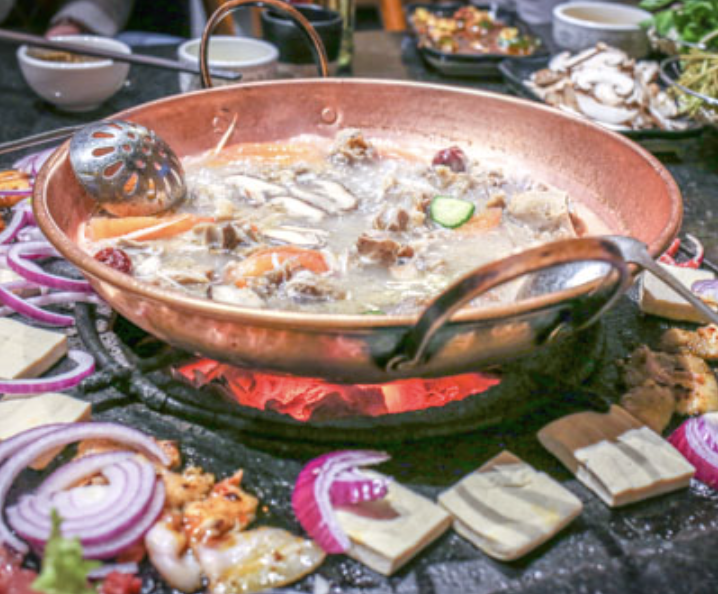 Tepanyaki grilling hot pot with vegetables and meat, surrounded by onion slices and tofu, on a stove with red embers.