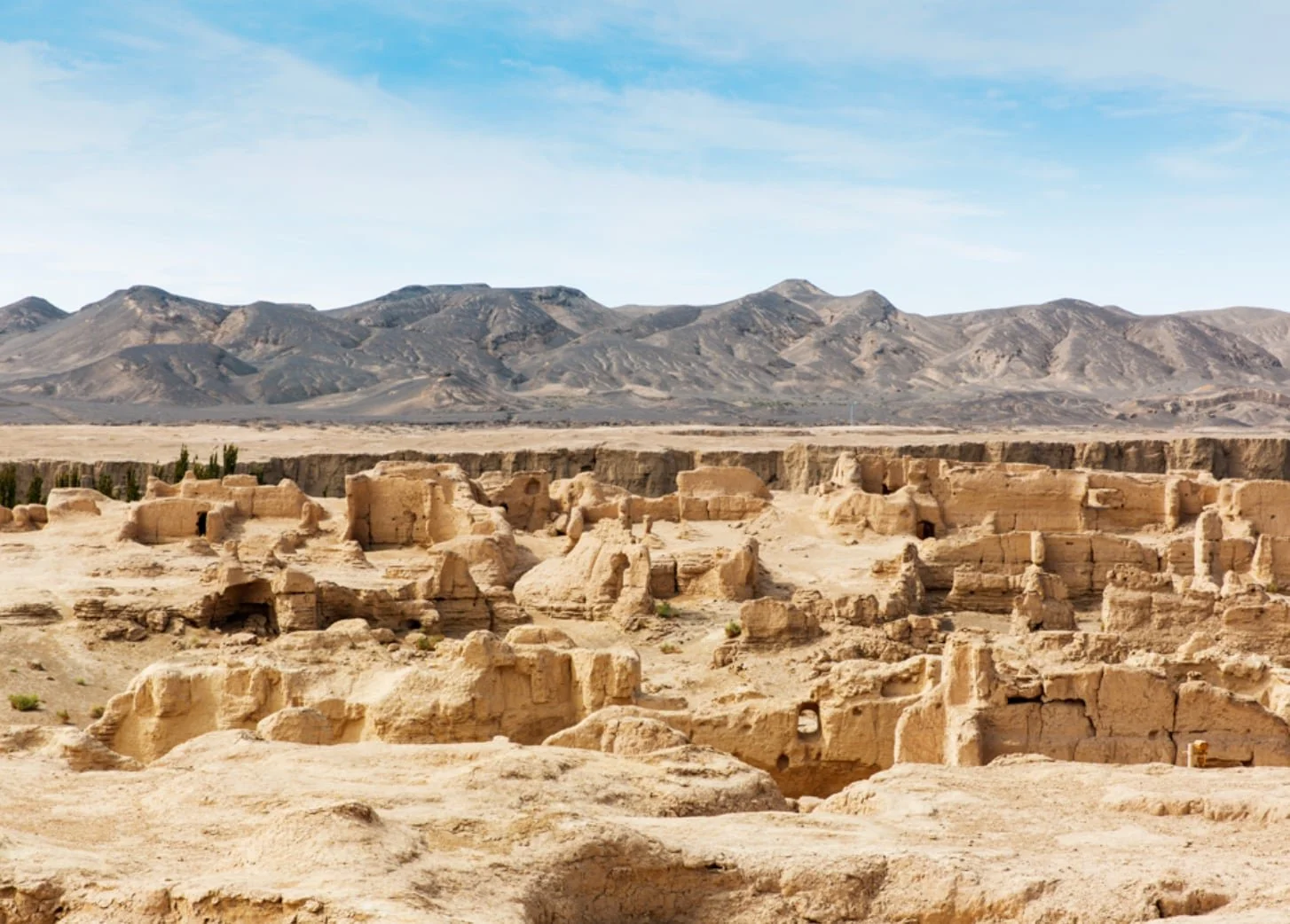 Ancient ruins in a desert landscape with mountains in the background and a clear blue sky.