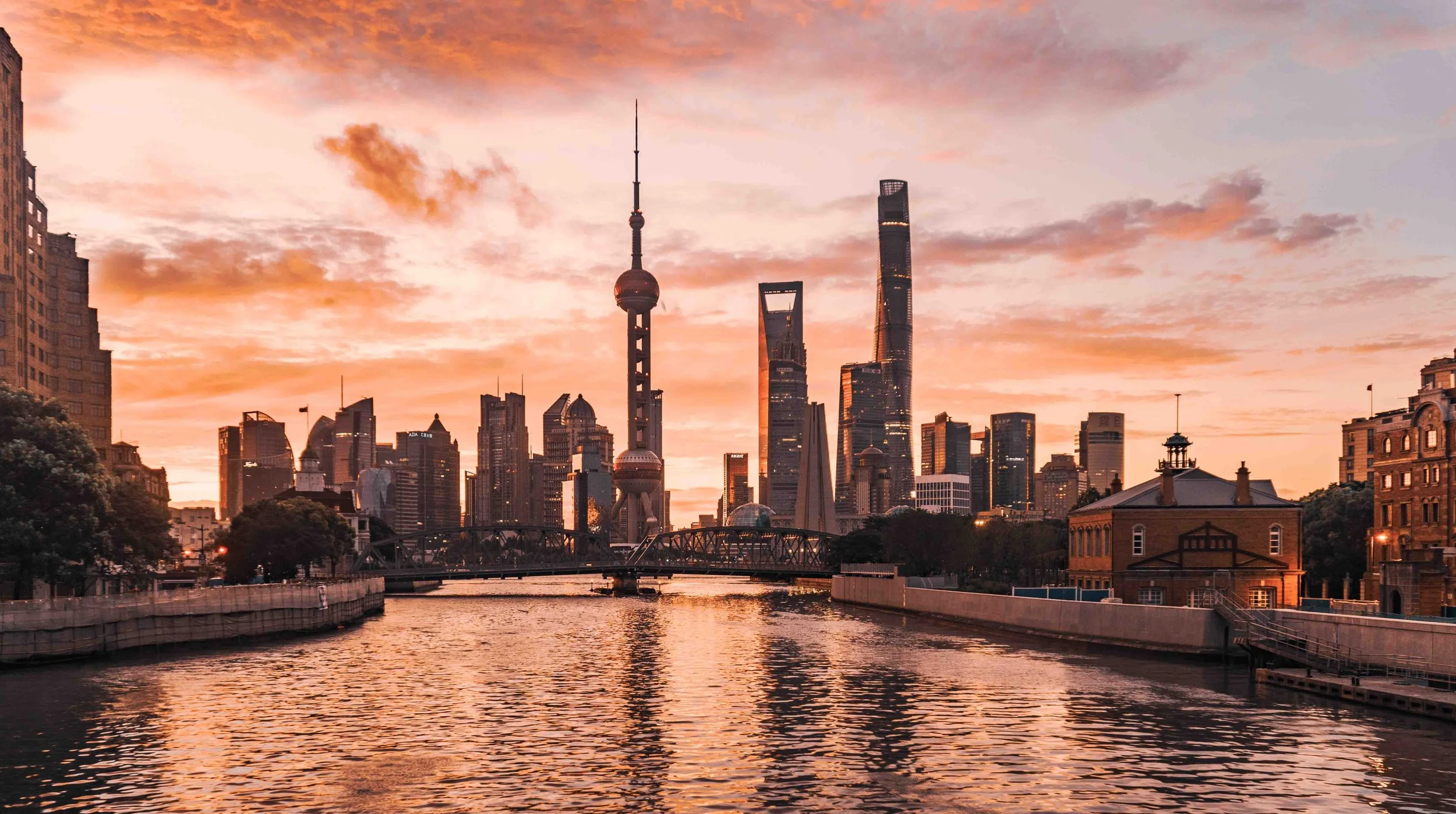 Shanghai skyline at sunset with tall skyscrapers and water in the foreground.