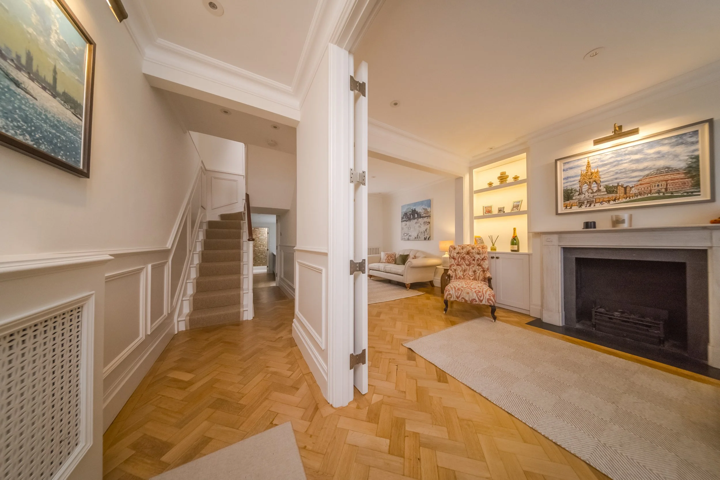 Living room with fireplace, artwork, built-in shelves, and seating area, viewed from hallway with staircase.