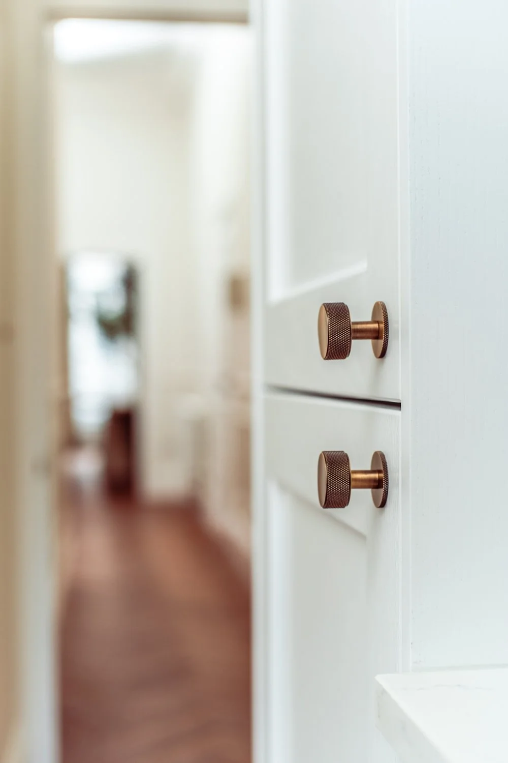 Close-up of white cabinet with two round, textured bronze knobs, seen in a well-lit room with blurred background.