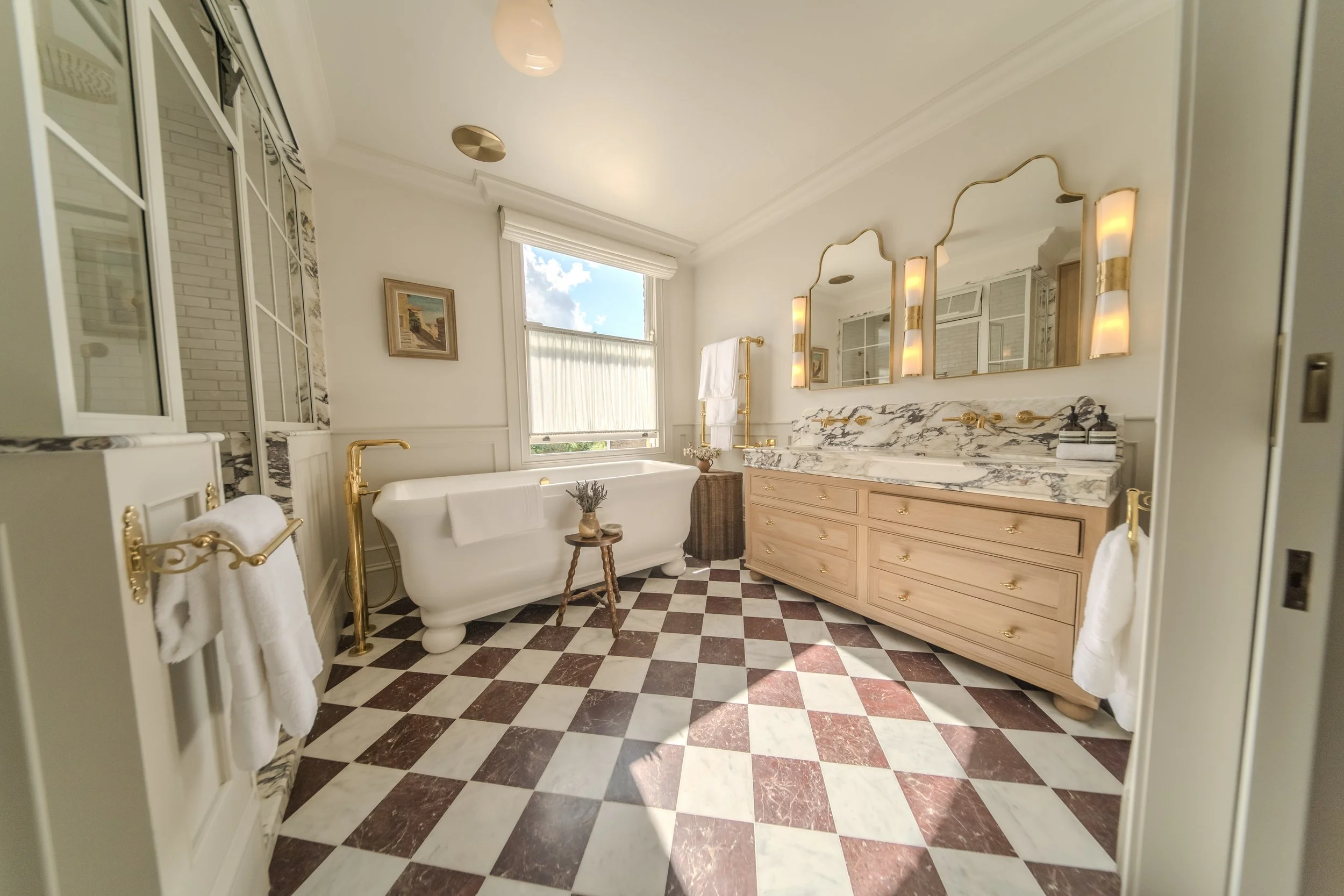 Jamie and Sophie Laing new home bathroom. Elegant bathroom with a clawfoot bathtub, a marble countertop with a large mirror, and checkered tile floor.