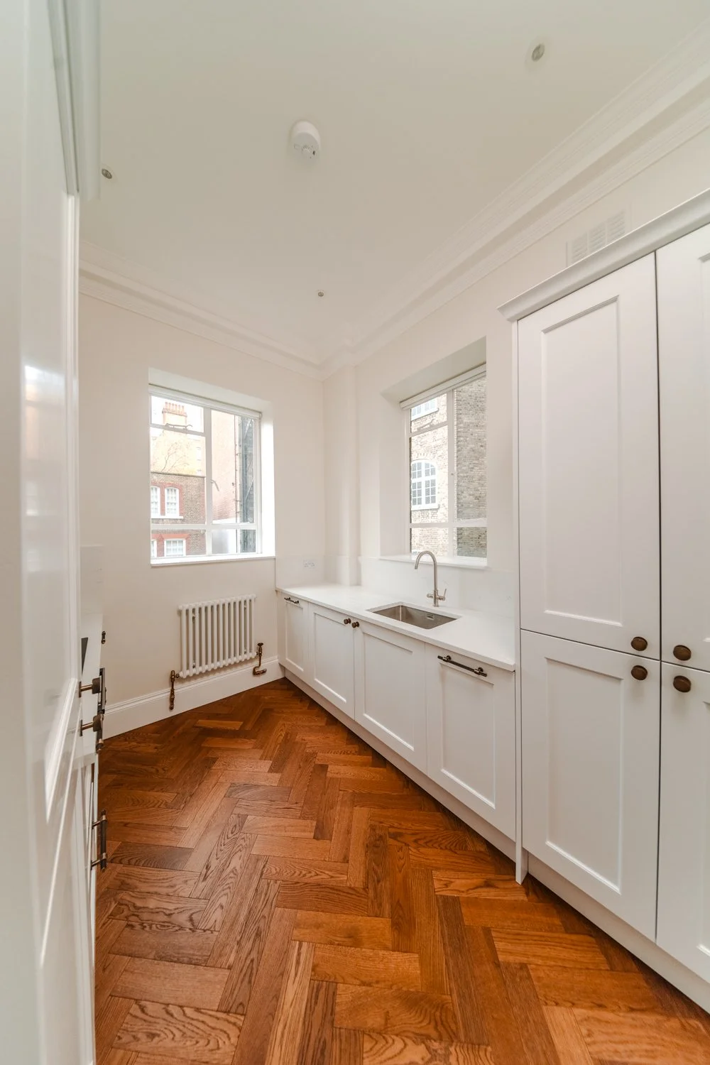 Kitchen with white cabinets, a window, a small sink, and wooden parquet flooring.