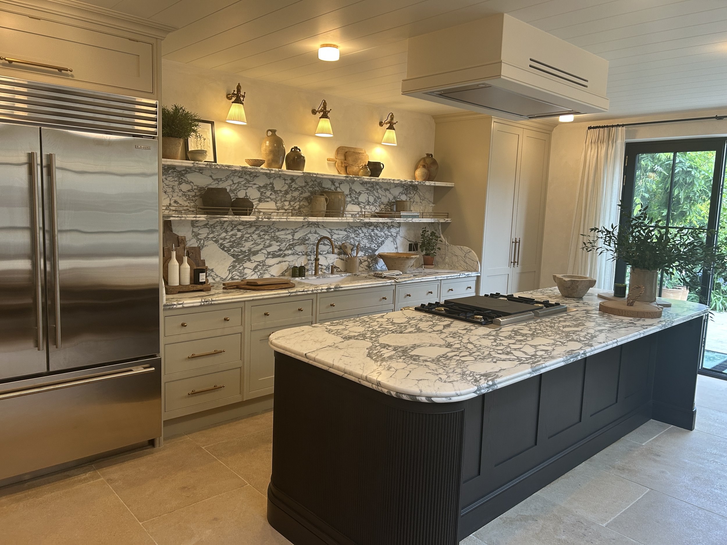 Modern kitchen with white cabinetry, black countertop, and a vintage black stove. The backsplash features beige and gray tile, and there are flowers in a glass vase on the island.