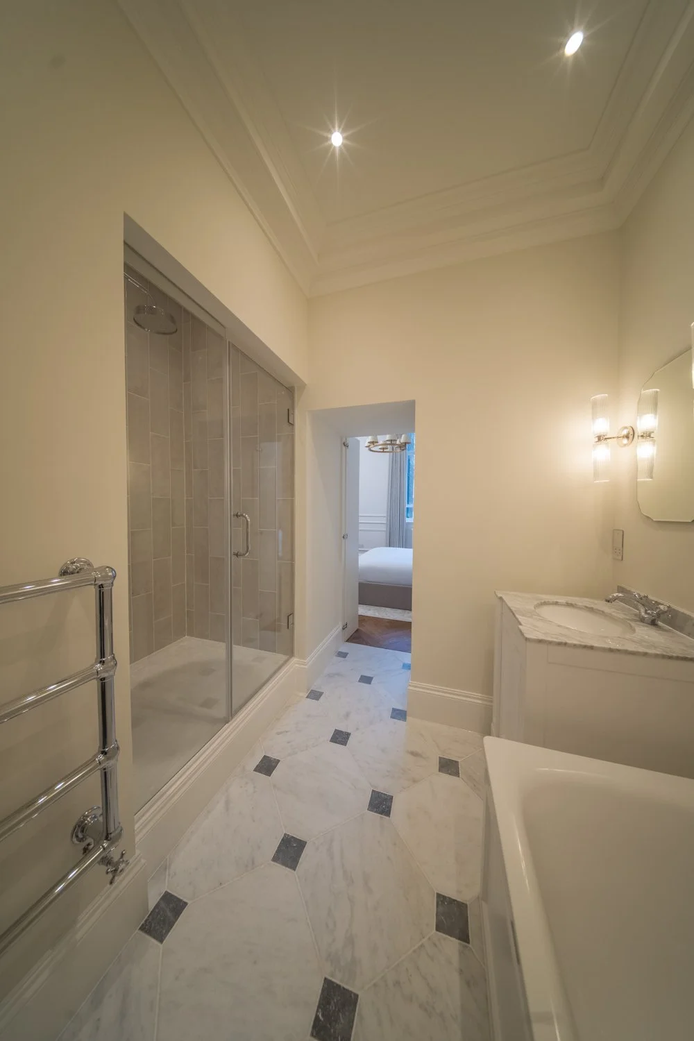 Luxurious bathroom with marble flooring, glass shower, bathtub, and elegant lighting fixtures.