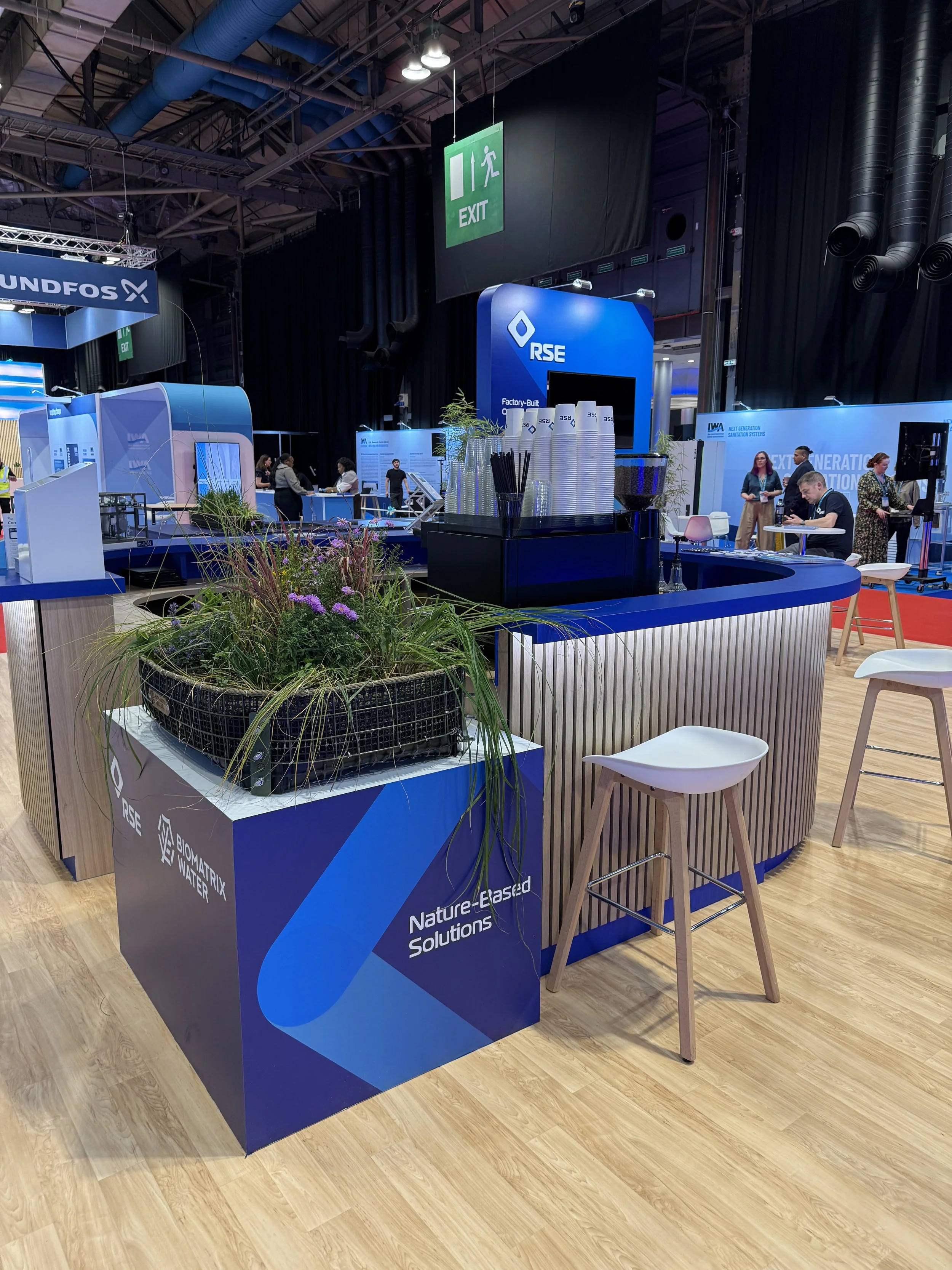 Curved wood-slatted coffee bar with RSE branded cups and Biomatrix Water nature-based solutions planter at the SEC Glasgow