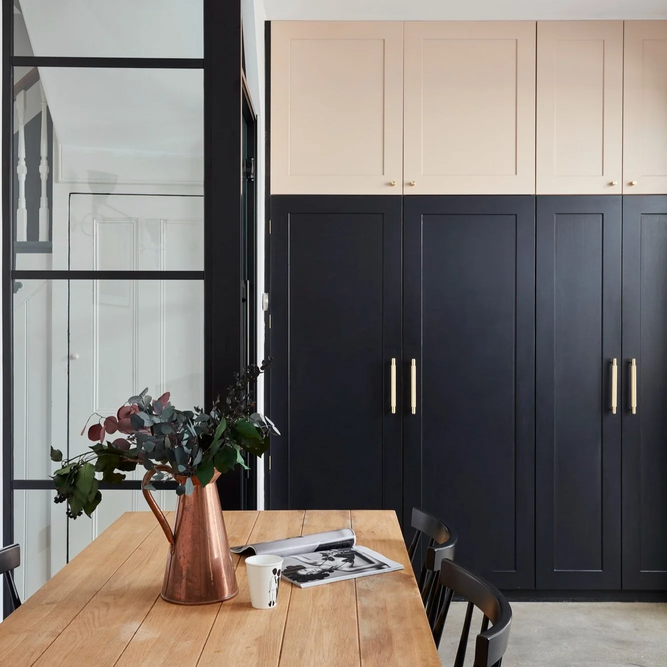 Modern kitchen with black cabinets, wooden table, copper vase with flowers, and an open magazine.