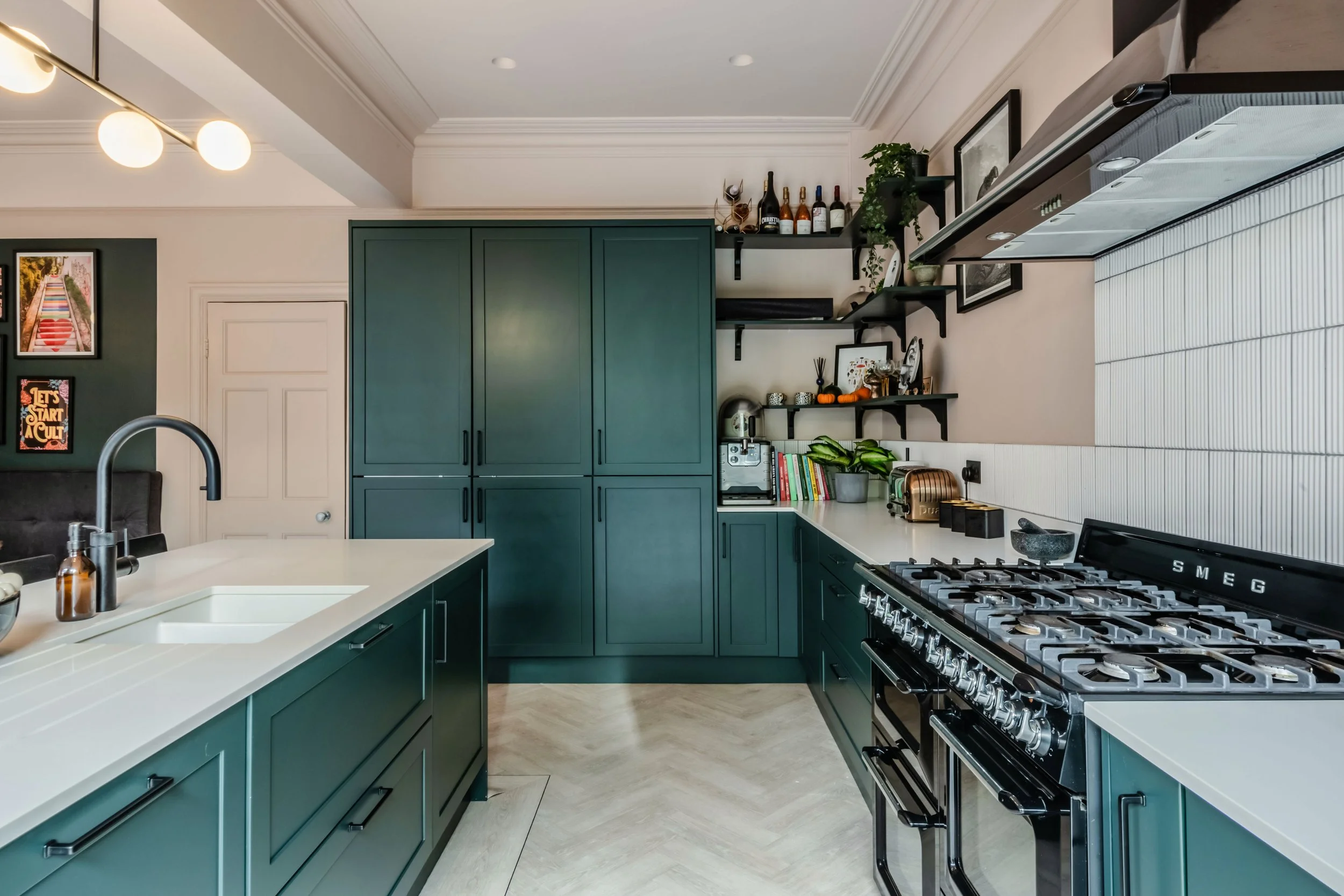 Modern kitchen with dark green cabinets, large stove, white countertops, and shelves with kitchenware and decor.