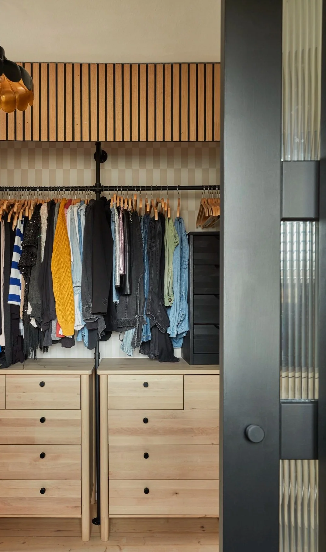 Modern closet with wooden drawers, hanging clothes on wooden hangers, and a sliding door partially open.