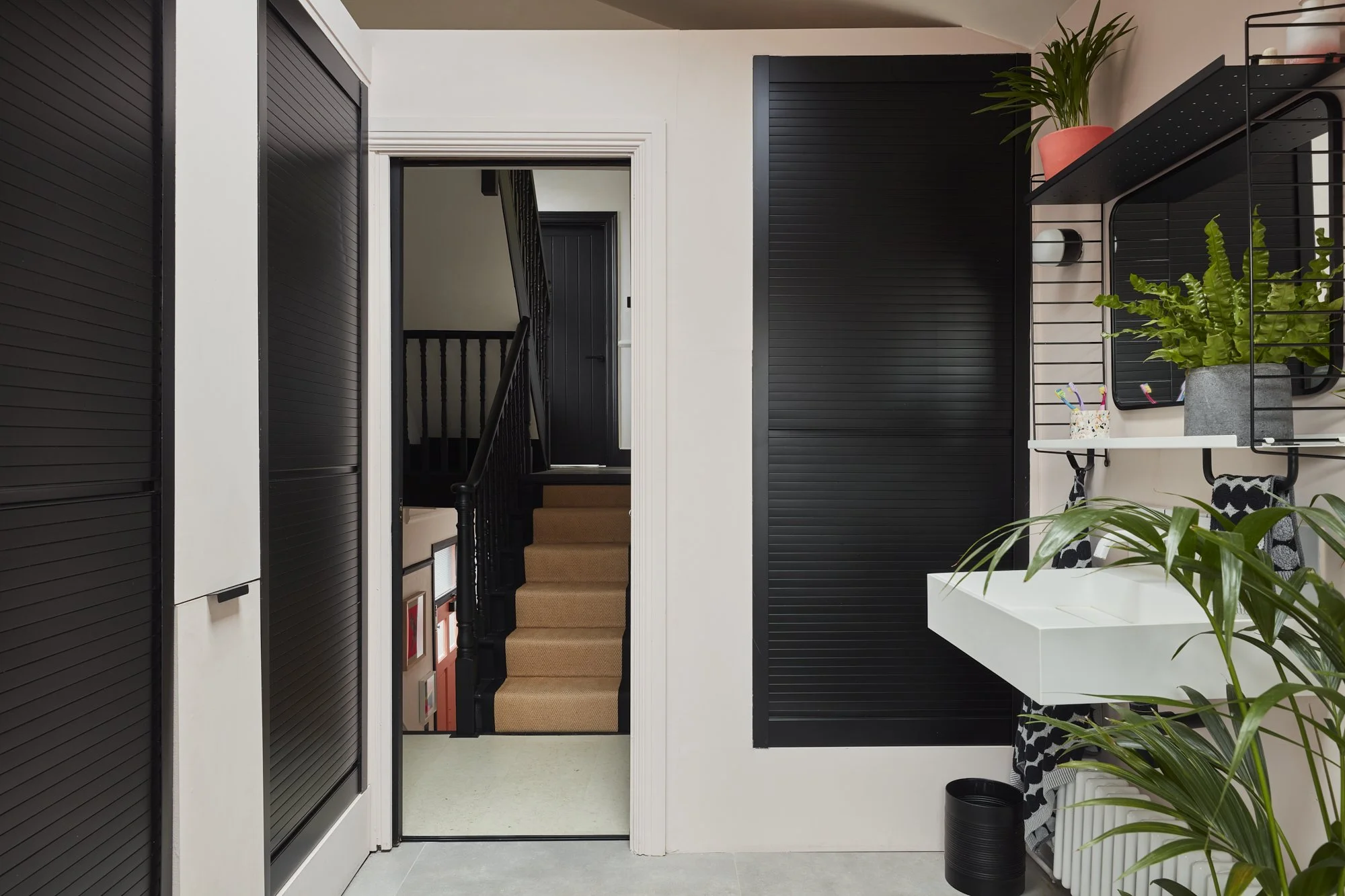 Modern interior with black sliding doors, white sink with plants, and a staircase in the background.