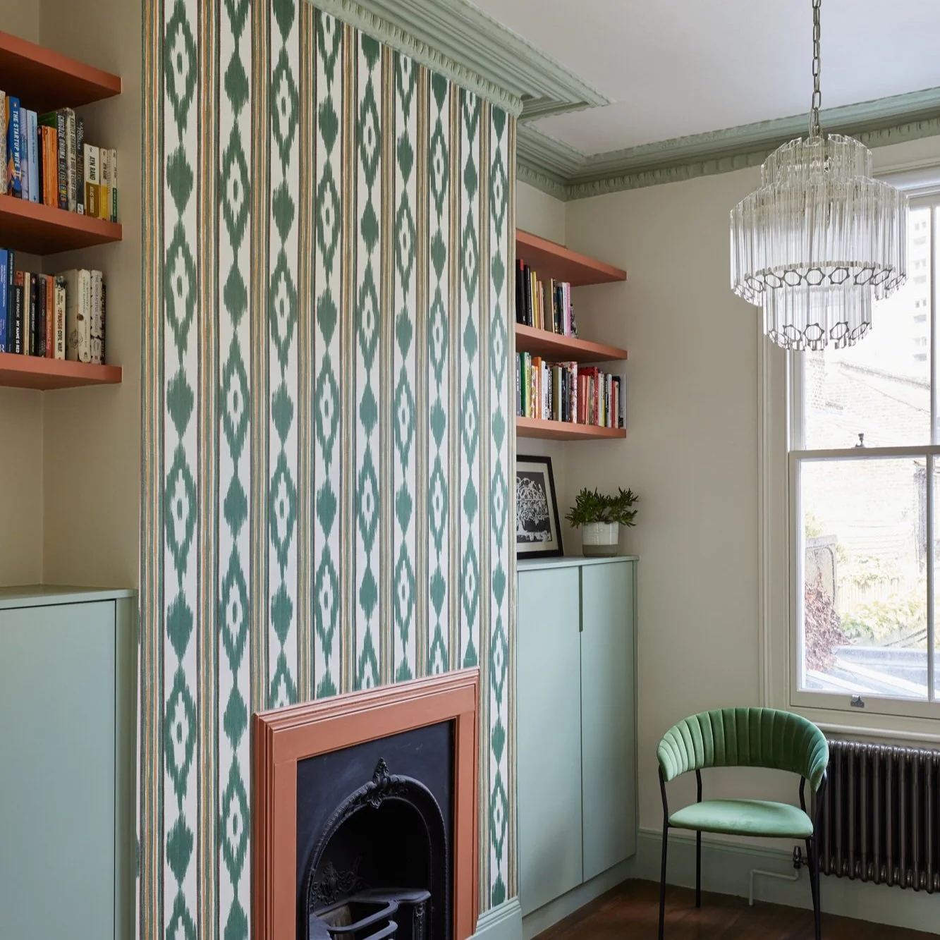 Room with patterned wallpaper, green fireplace, bookshelves, chandelier, and green chair